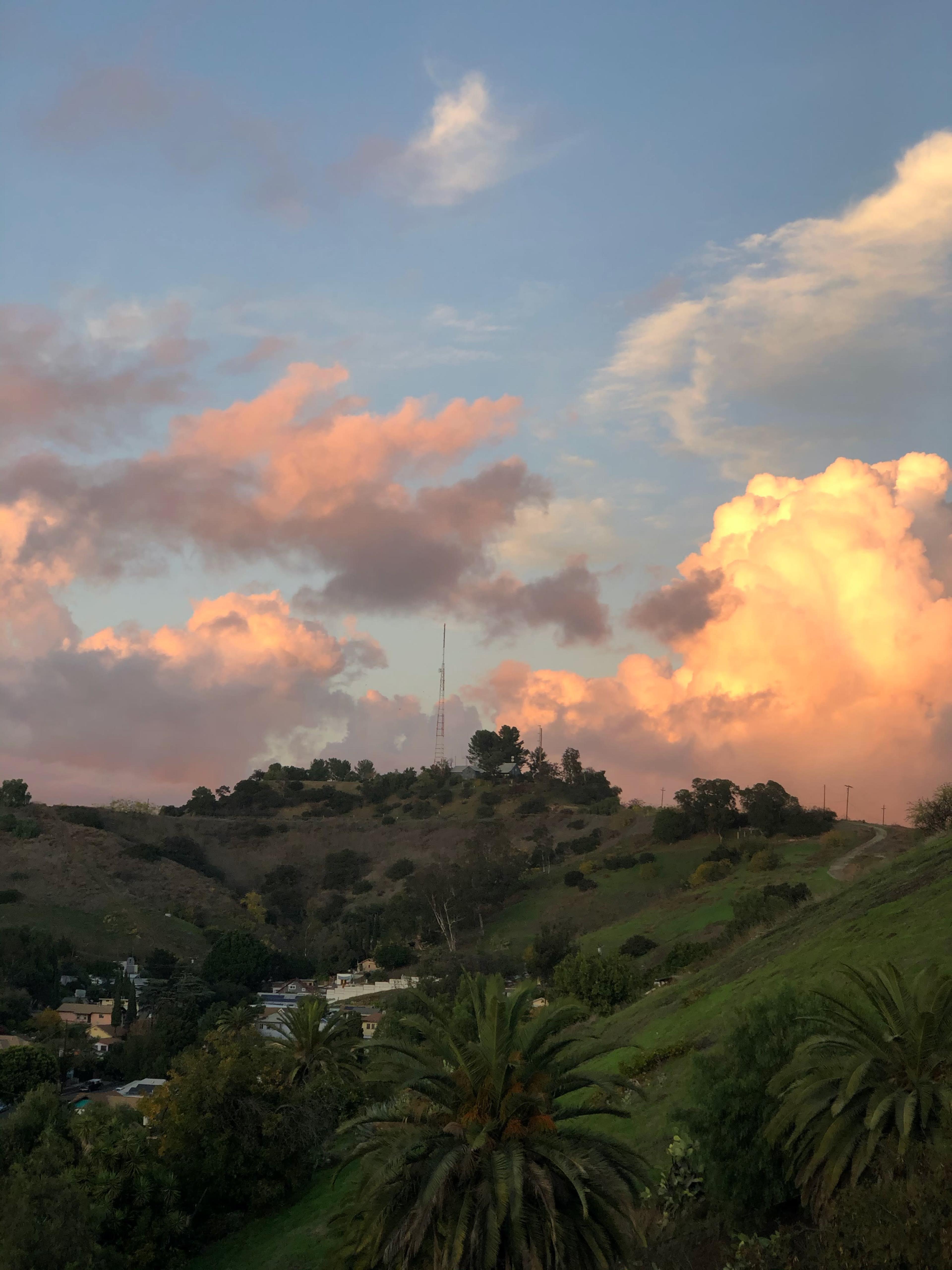 A telecommunications tower rises above rolling green hills under a colorful sky filled with clouds.