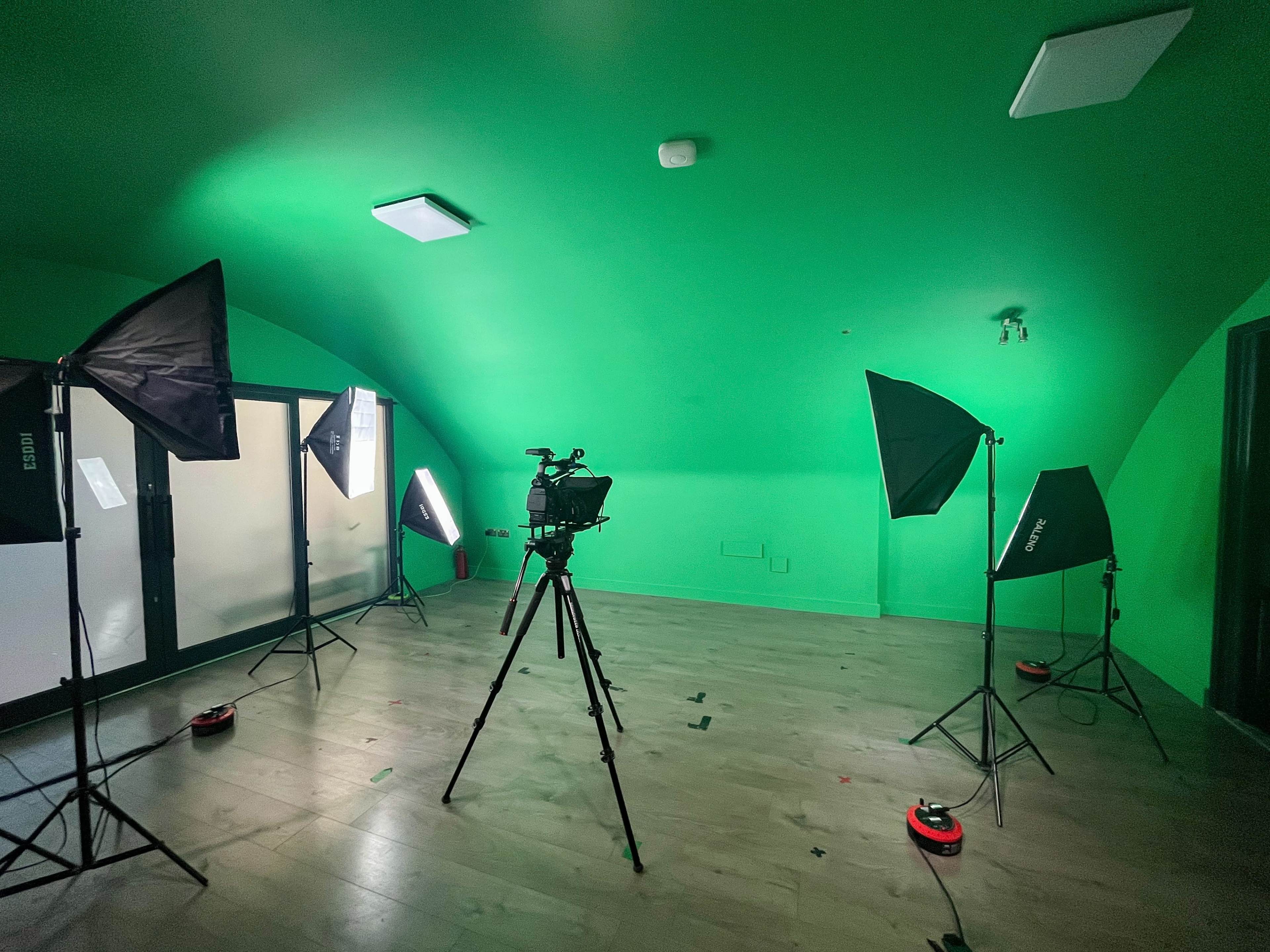 A green studio room is set up with lighting equipment and a camera on a tripod.