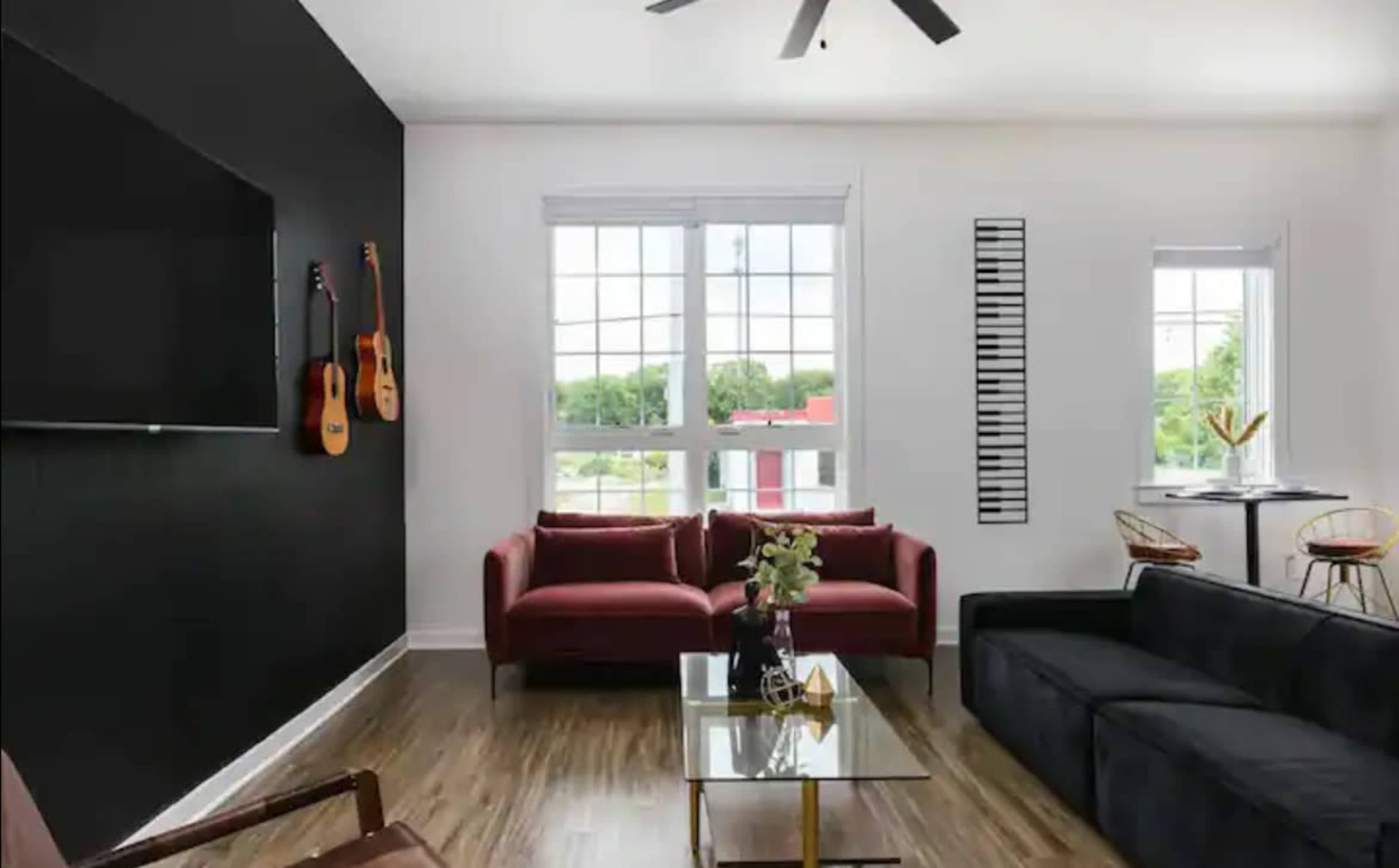 A modern living room with two sofas, a glass coffee table, and decor including guitars on the wall and a piano keyboard panel.
