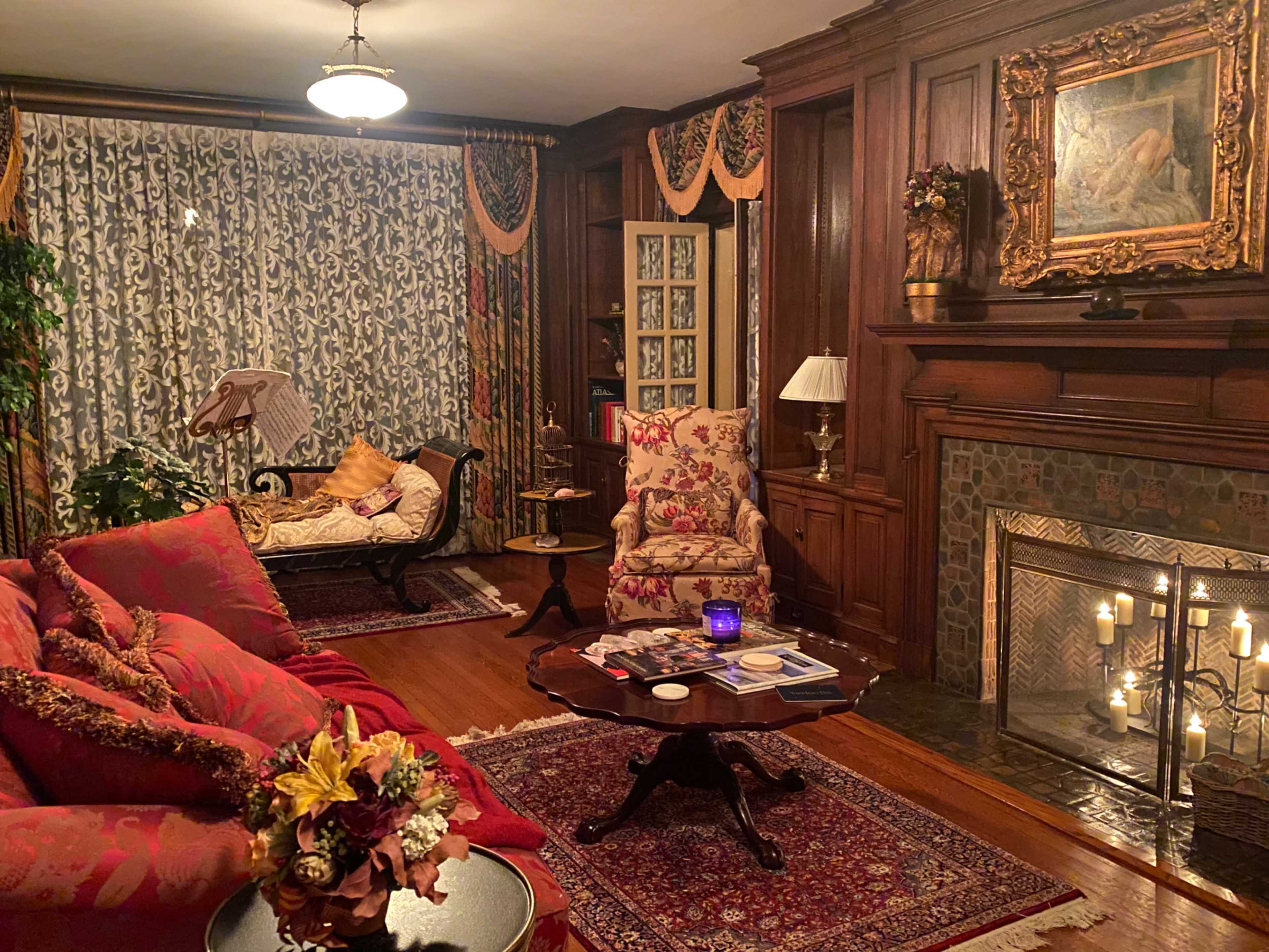 The image shows a cozy living room with floral upholstered furniture, a wooden fireplace, and decorative curtains.