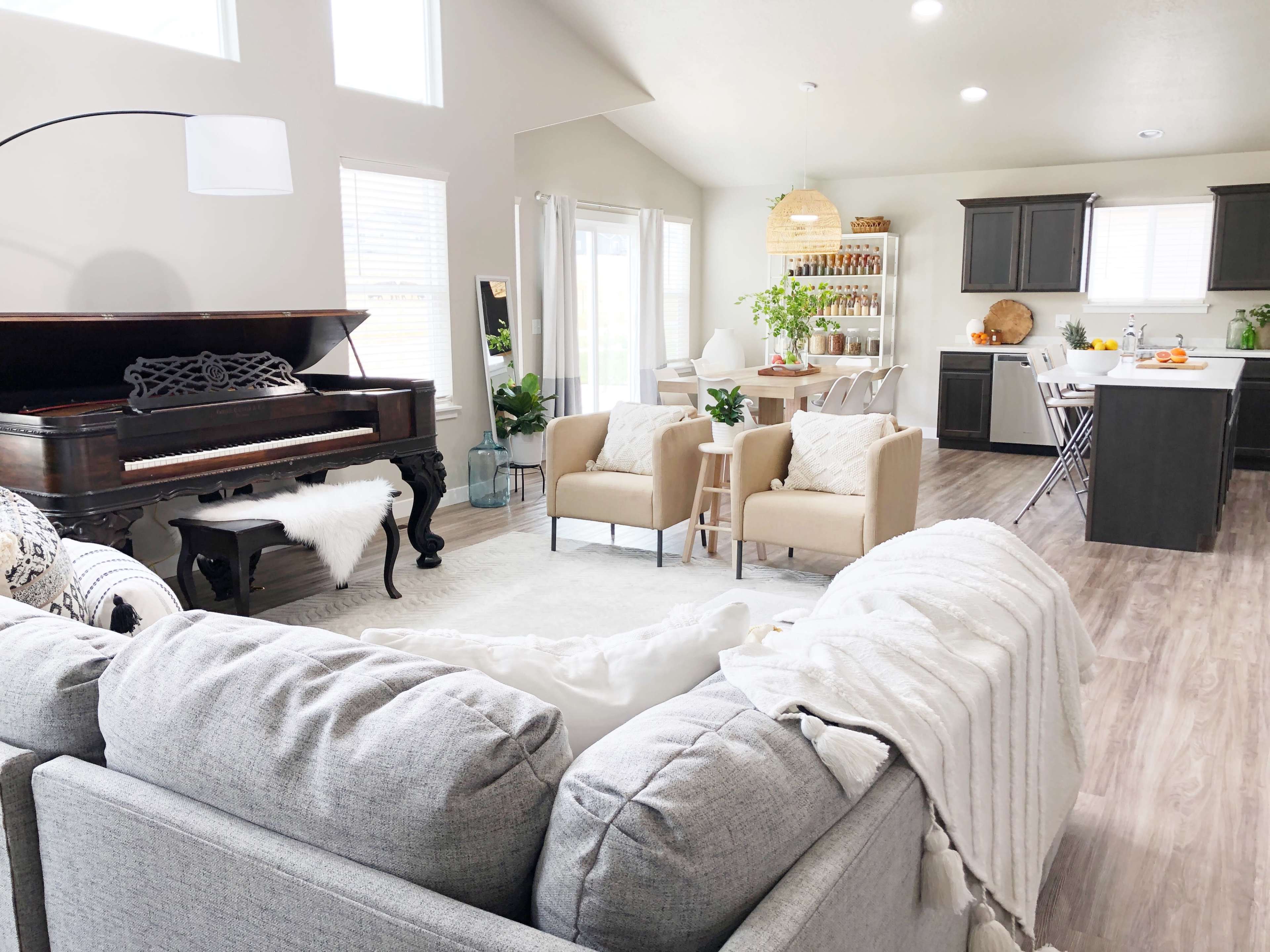 A modern open-concept living area that includes a piano, two armchairs, a sectional sofa, and a kitchen with dining space.