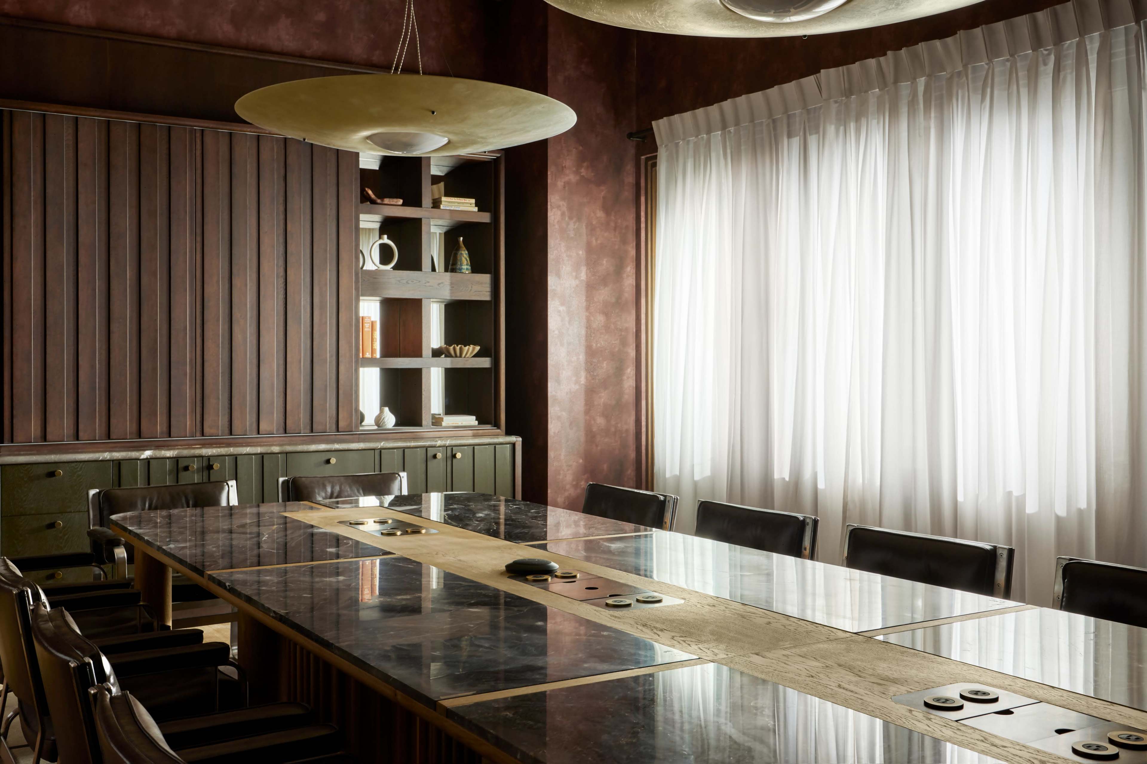 The image shows a modern conference room with a large rectangular table, surrounded by black chairs, and a window covered by white drapes.