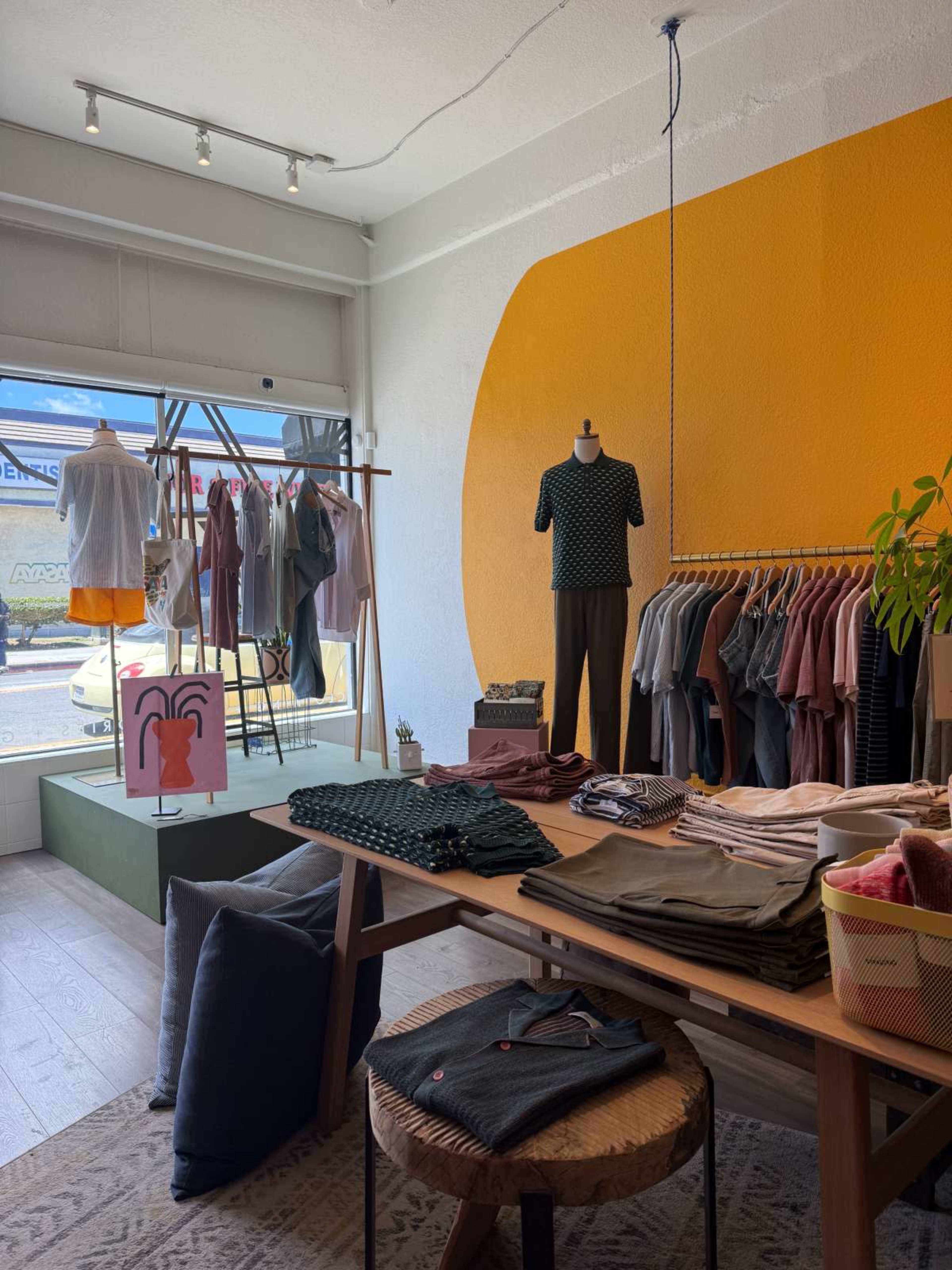 The image shows a clothing store interior with a display of hanging garments, a table with folded clothes, and a vibrant orange wall.