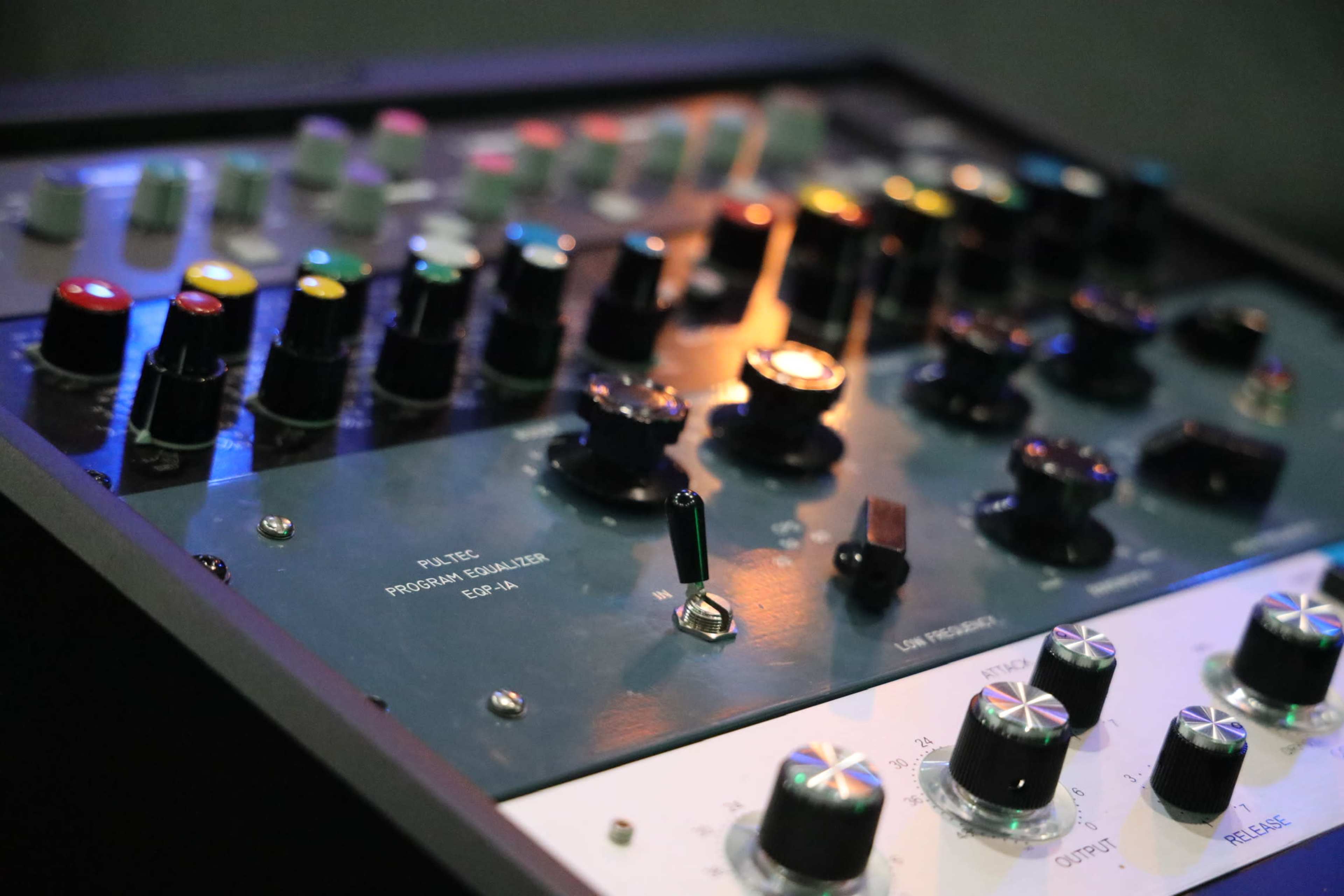 A close-up of a professional audio mixing console with various colorful knobs and sliders.