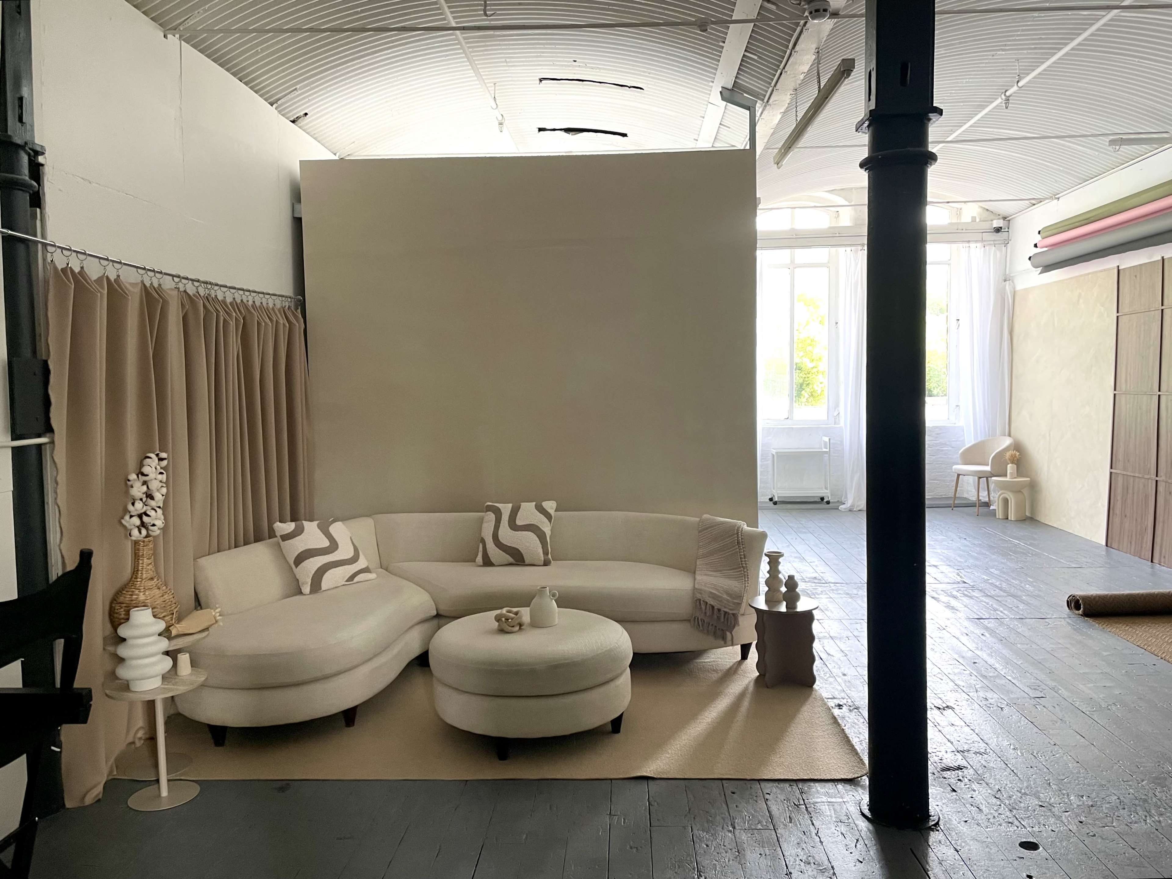 The image shows a spacious room with a curved white sofa, a light-colored rug, and minimal decor, including a small table and chair.