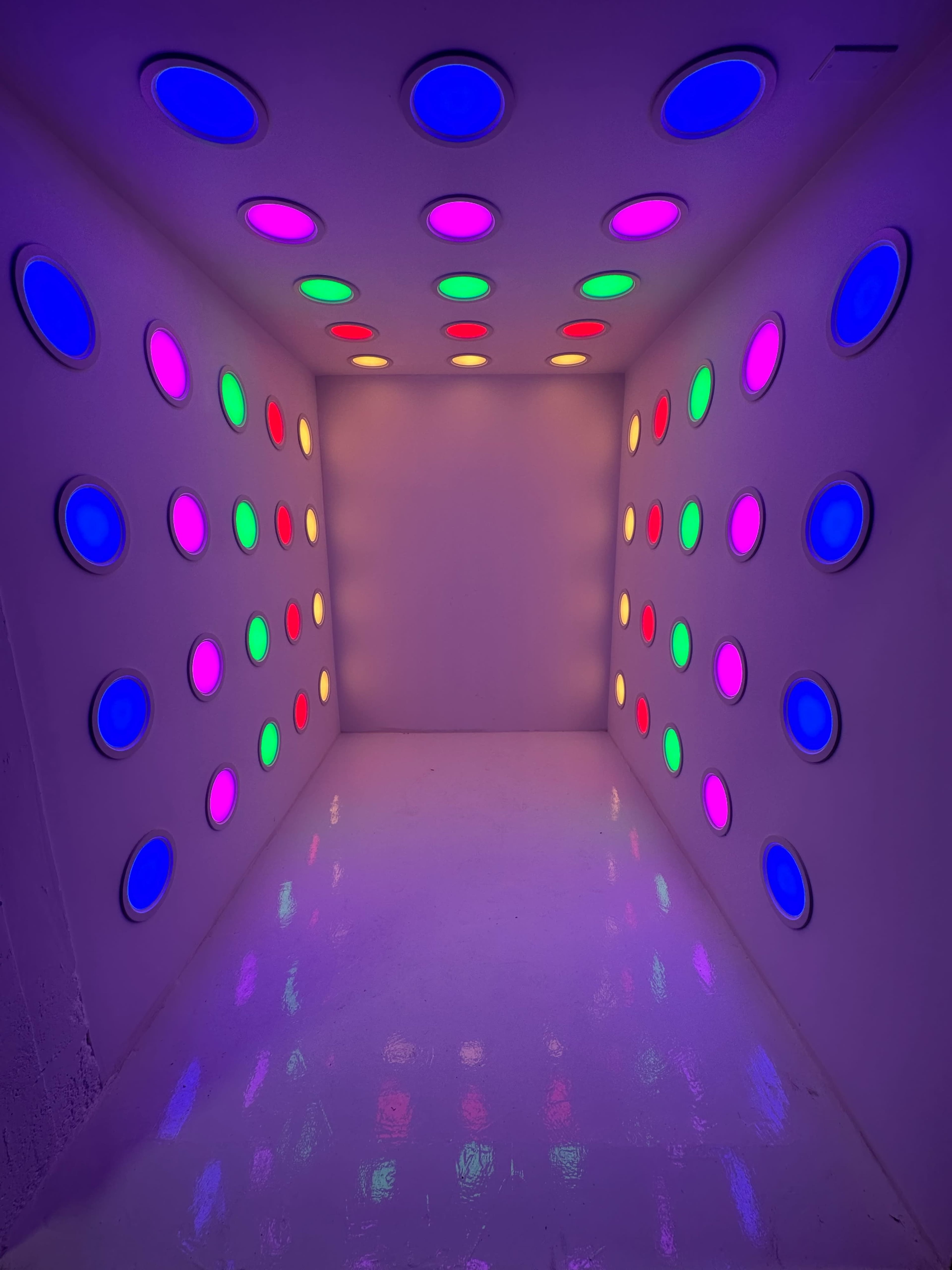 A brightly lit room with a white floor and walls adorned with circular lights in various colors, including pink, green, and purple.
