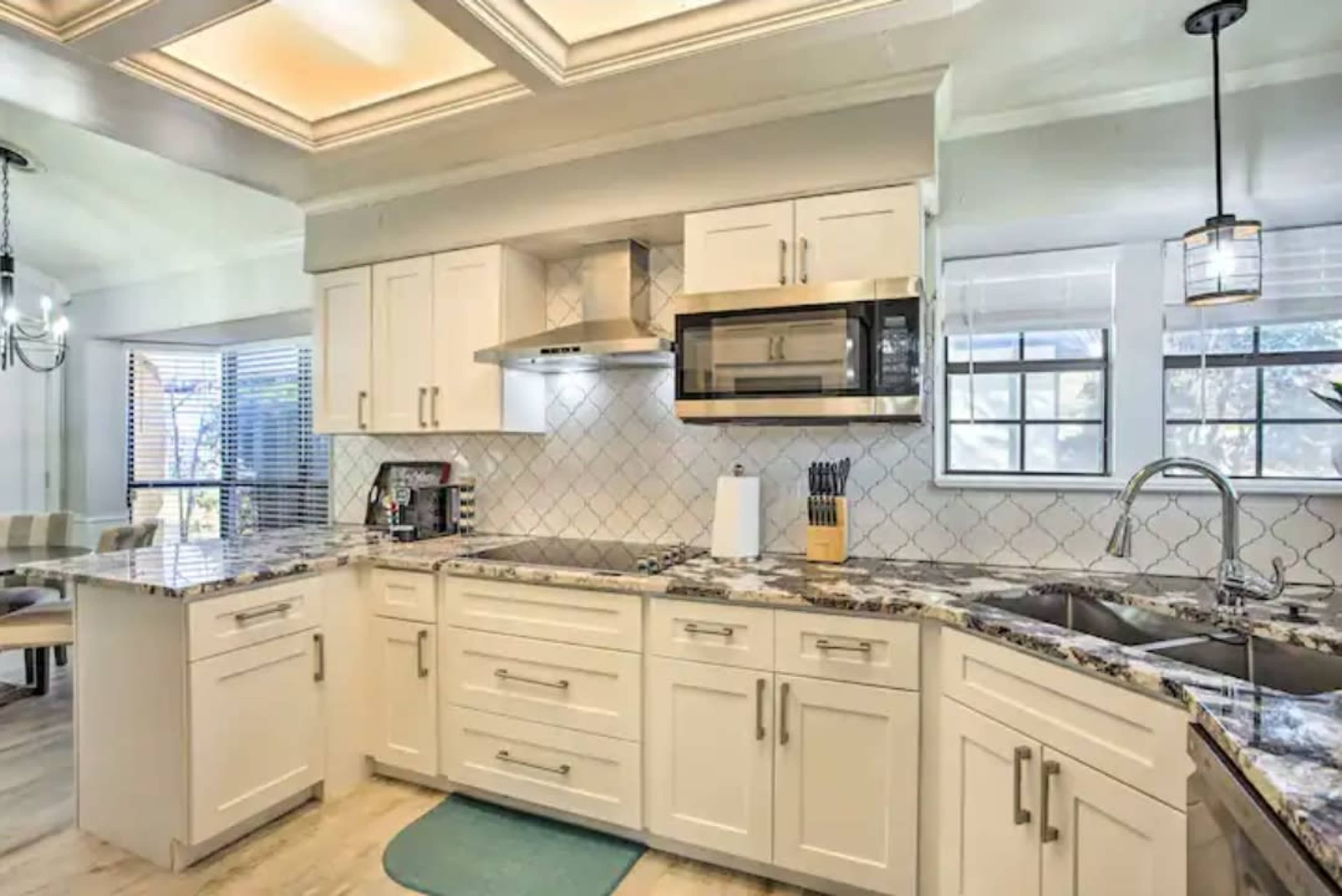The image shows a modern kitchen featuring white cabinetry, stainless steel appliances, and a marble countertop.