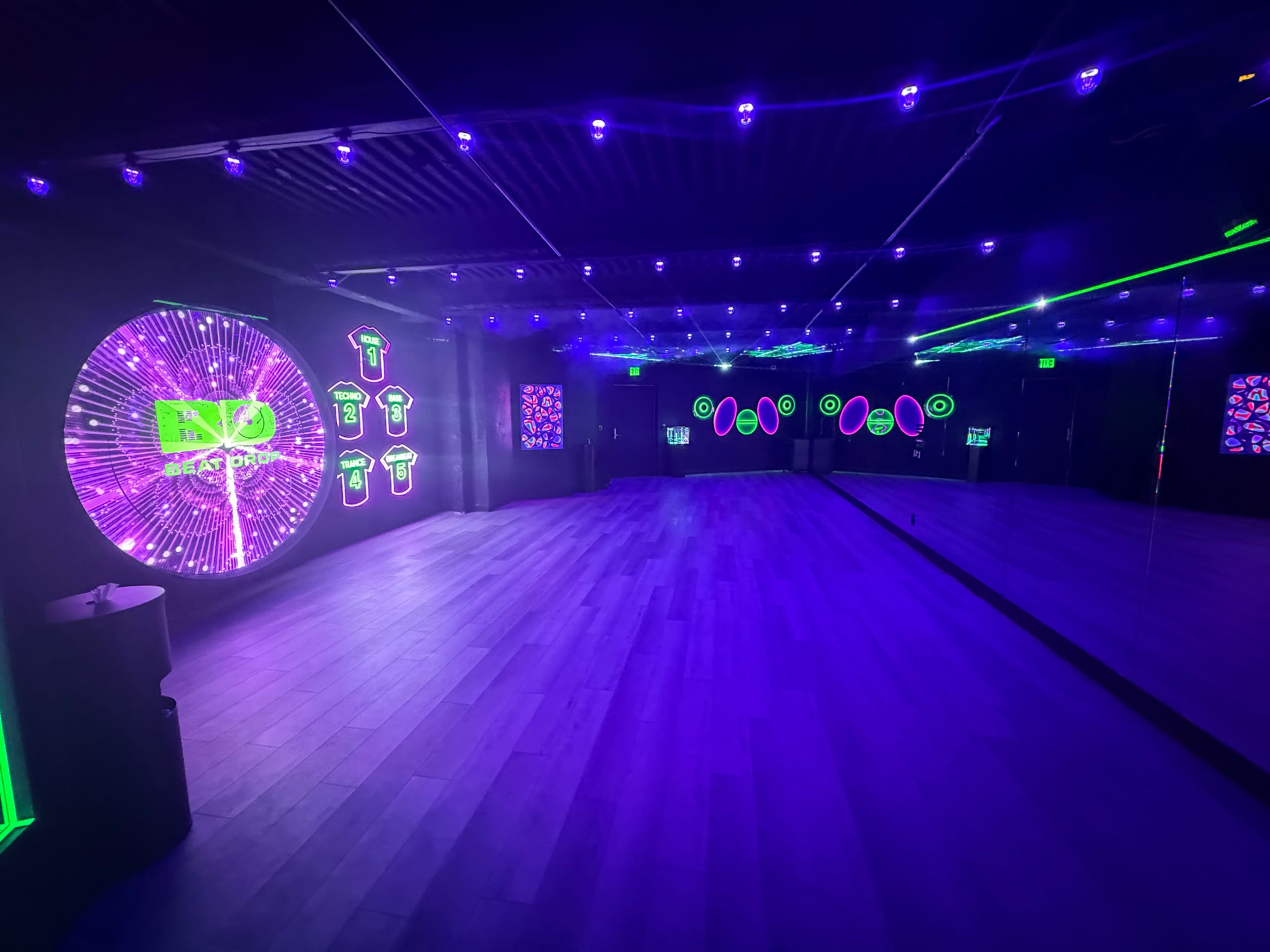 The image shows a dimly lit dance studio with neon lights and a large circular display on one wall.
