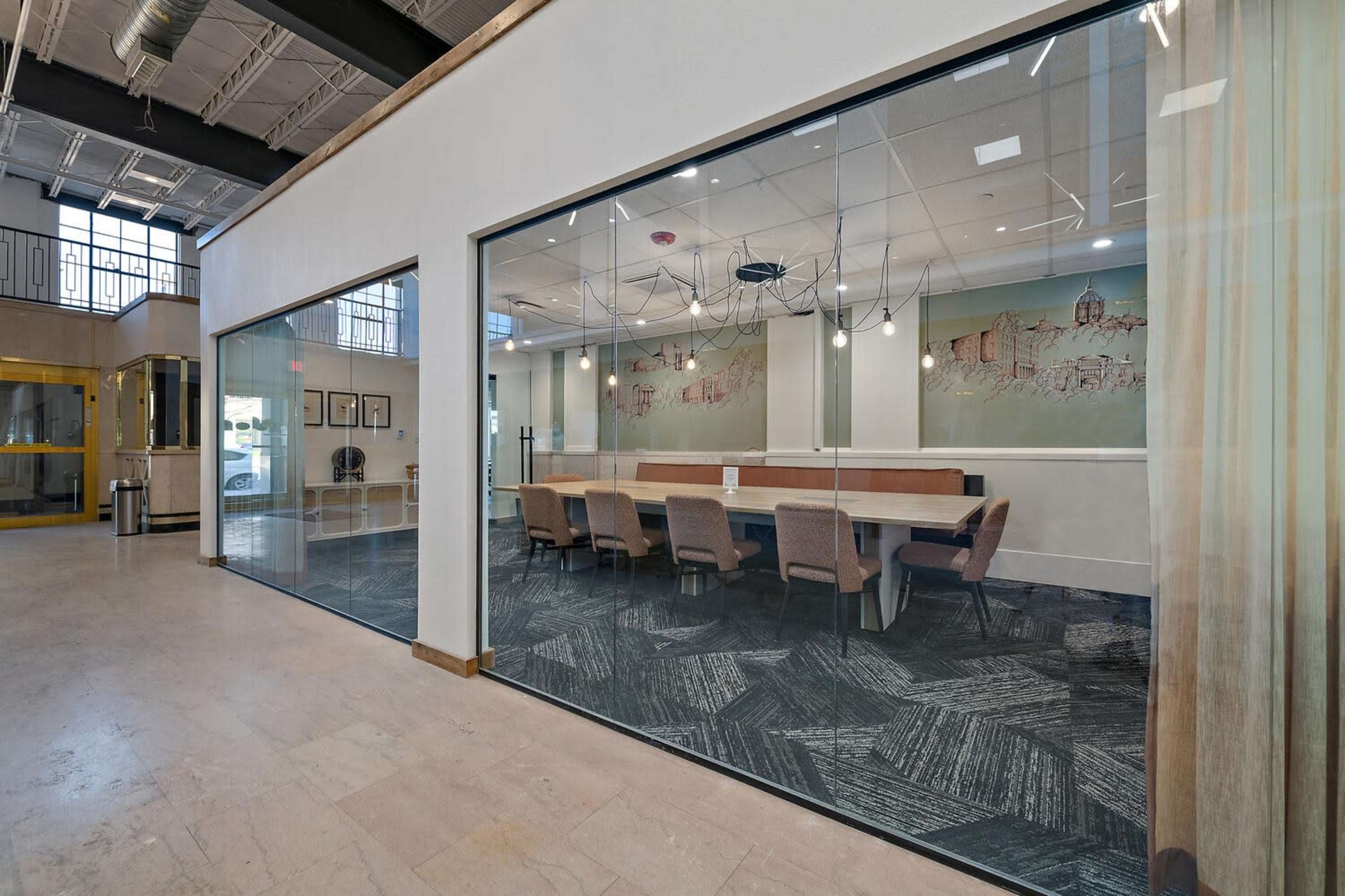 The image shows a modern office space featuring glass walls, a long conference table with chairs, and decorative wall art.