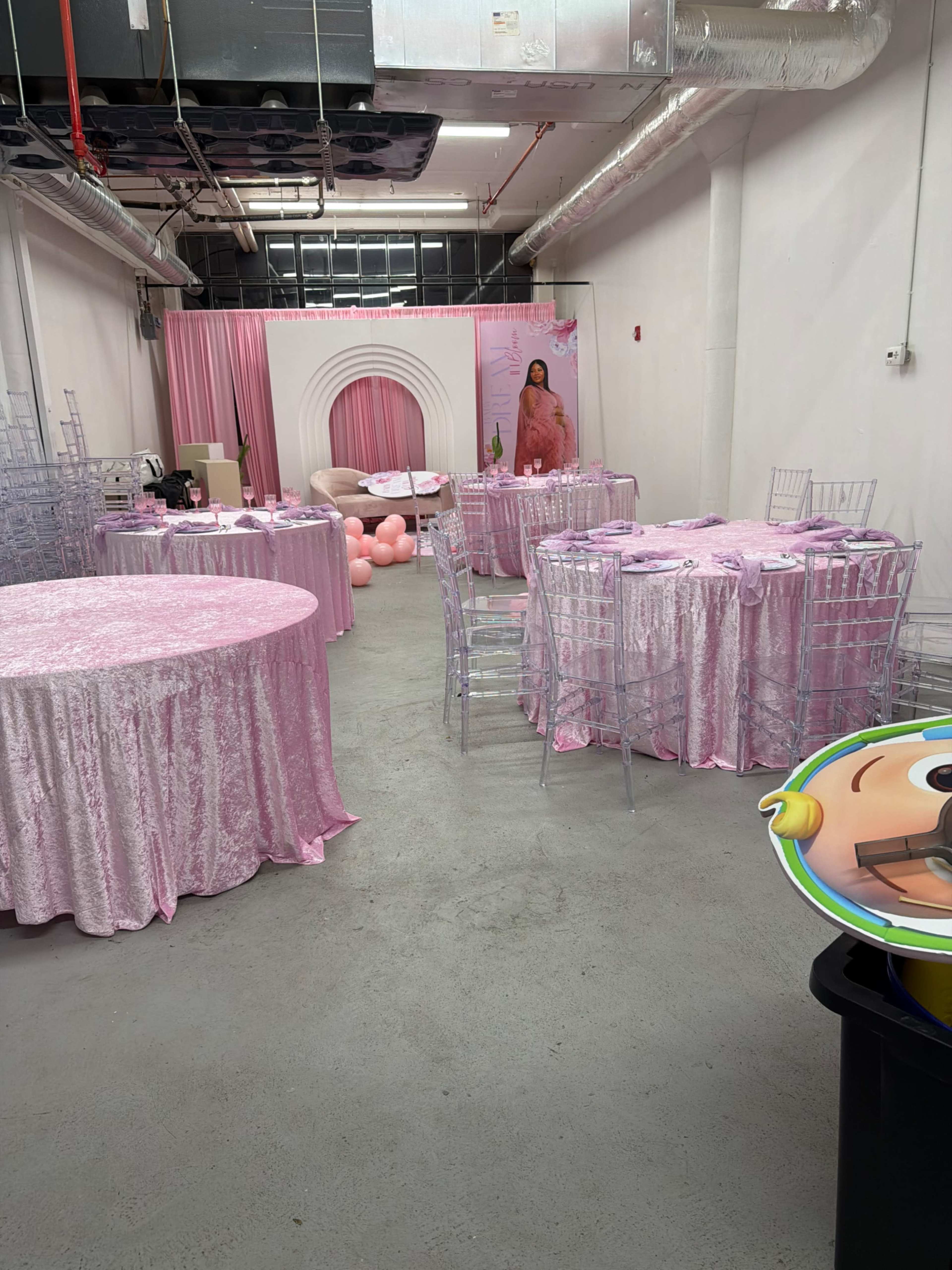 The image depicts a party venue with pink velvet tables, clear acrylic chairs, and decorative elements including balloons and a backdrop featuring a model.