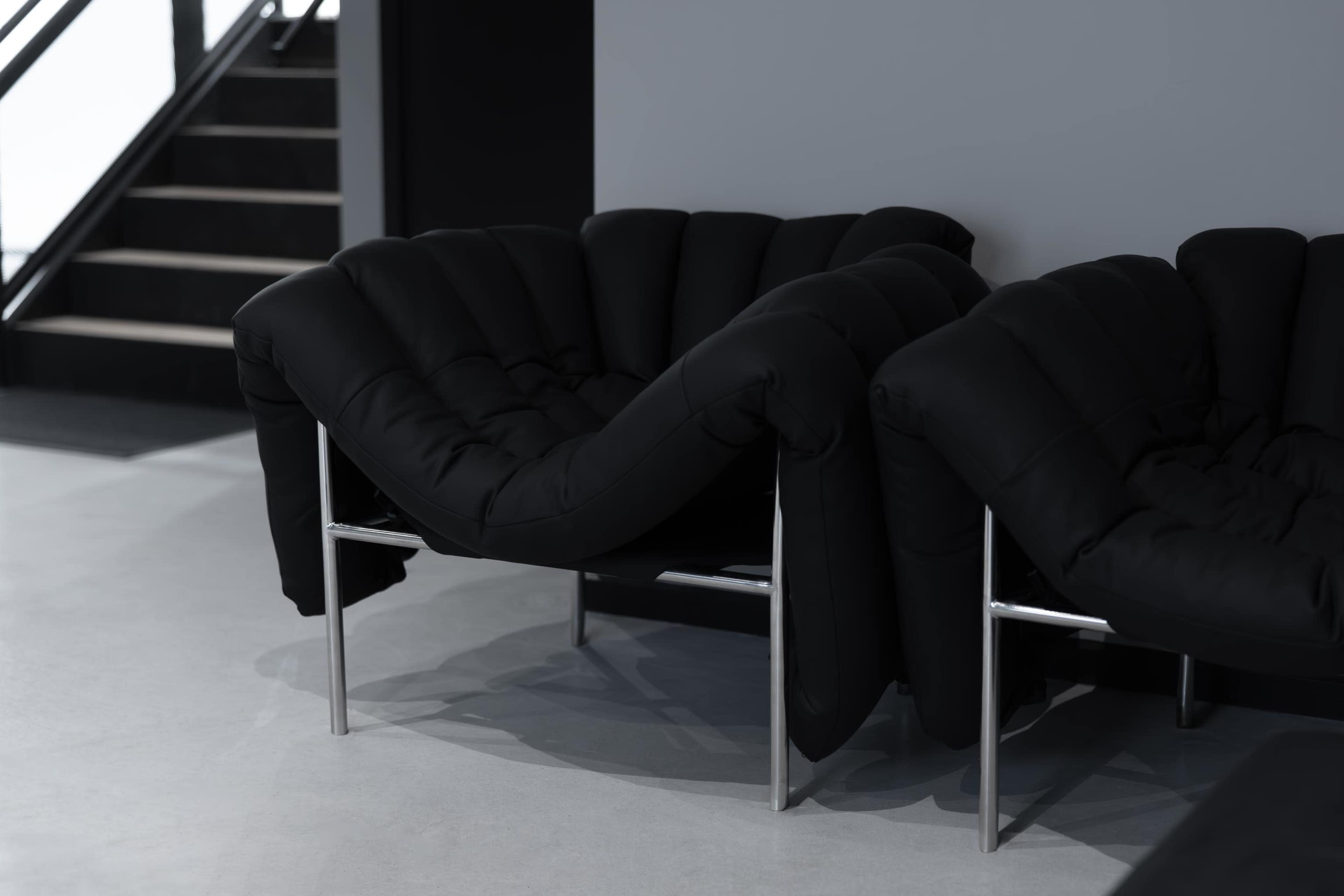 Two modern black upholstered chairs with silver metal frames are positioned next to each other in a minimalist interior space.