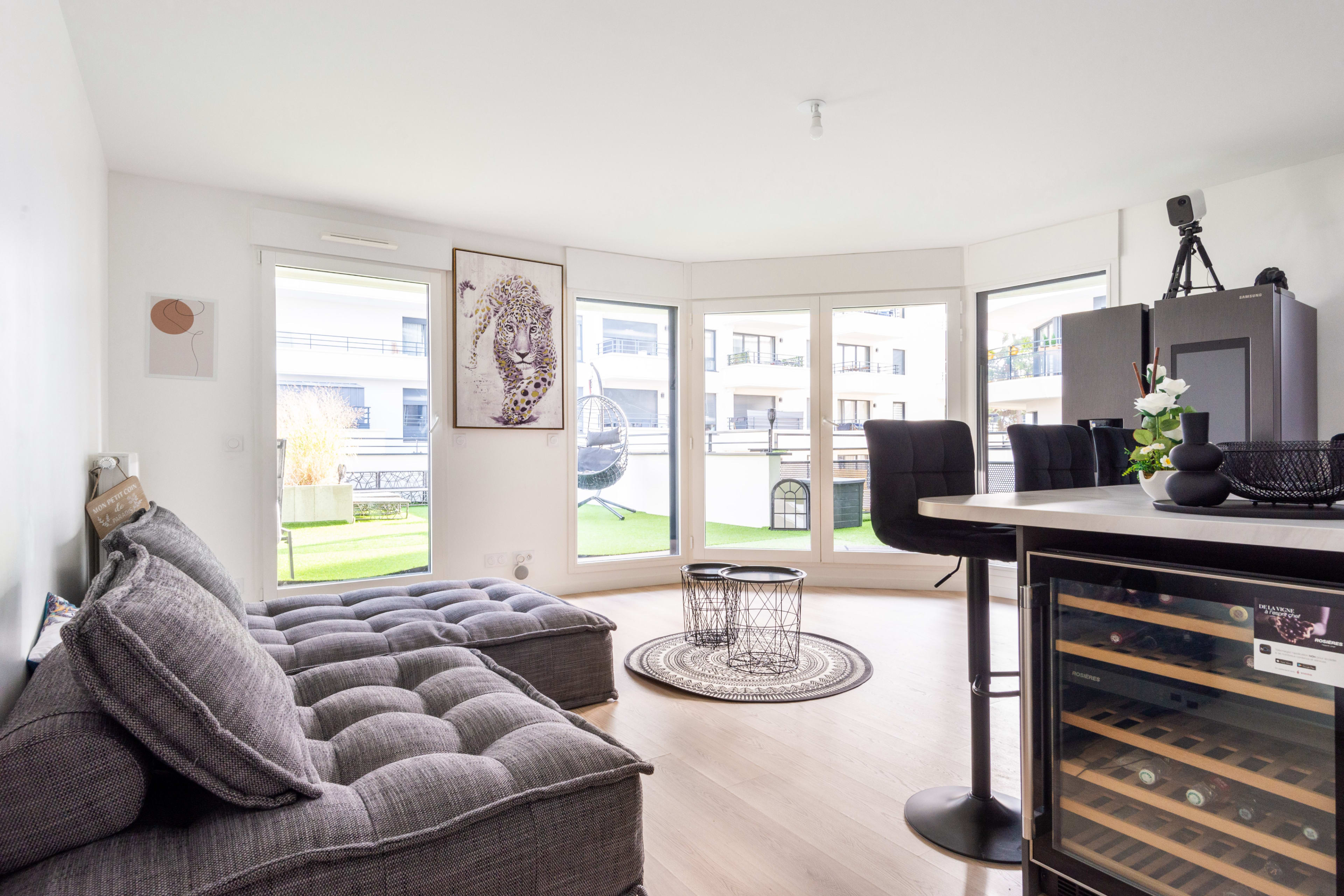 A modern living space with a gray upholstered sofa, a round rug, and a view of a green outdoor area through large windows.