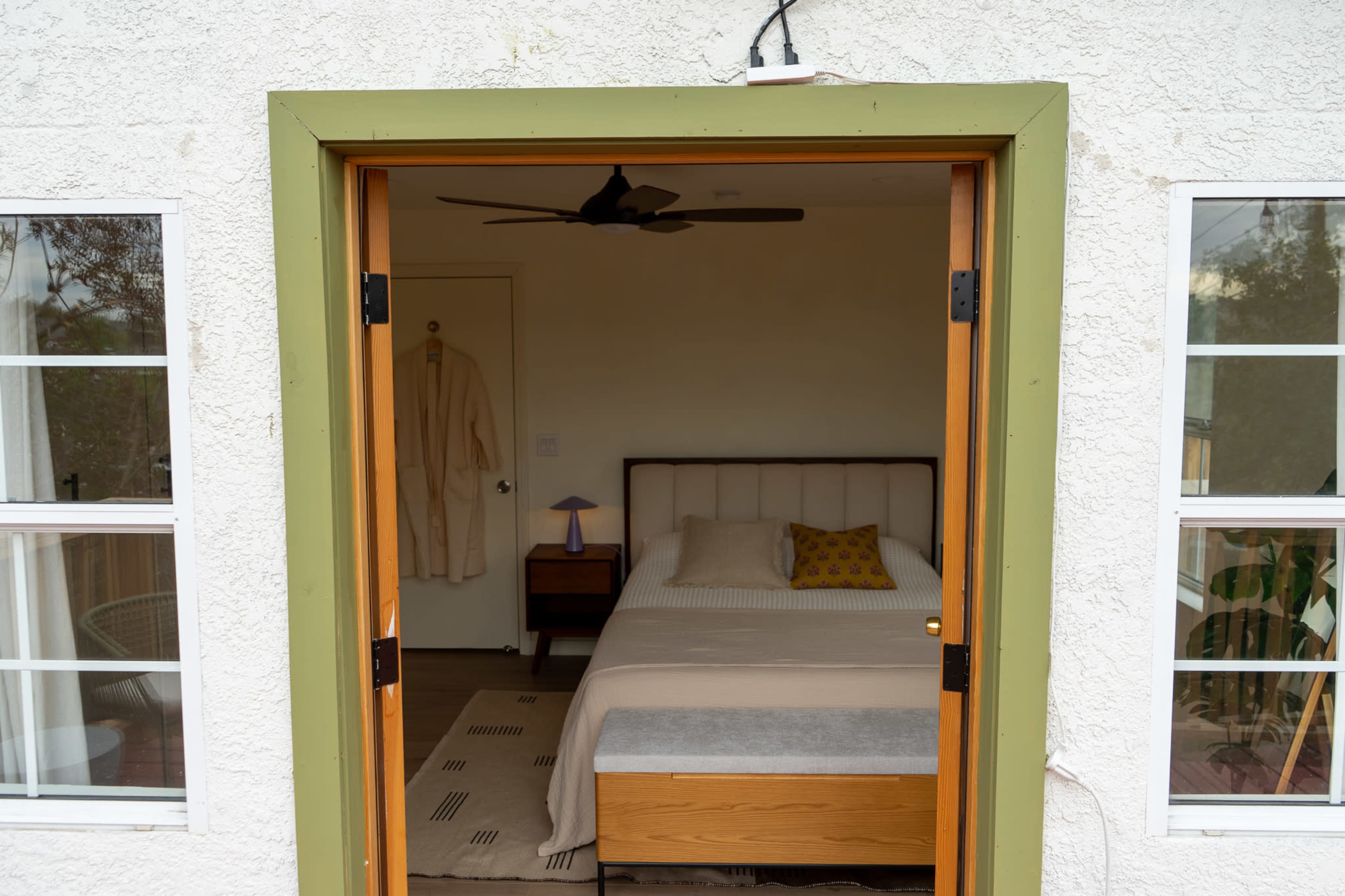A cozy bedroom is visible through an open doorway, featuring a bed with a light-colored bedspread and a nightstand beside it.
