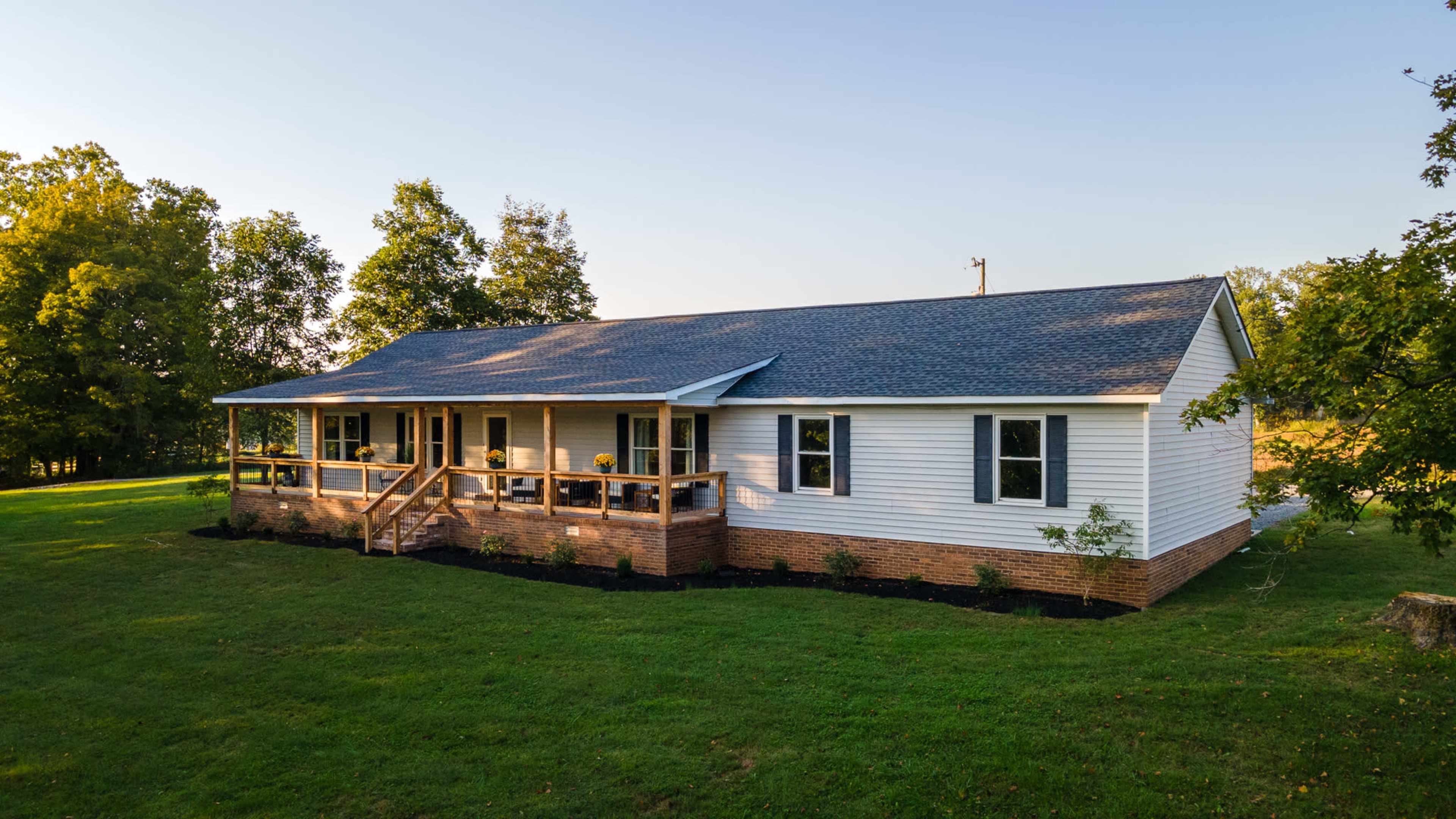 A single-story, white house with a porch sits on a grassy lawn surrounded by trees.
