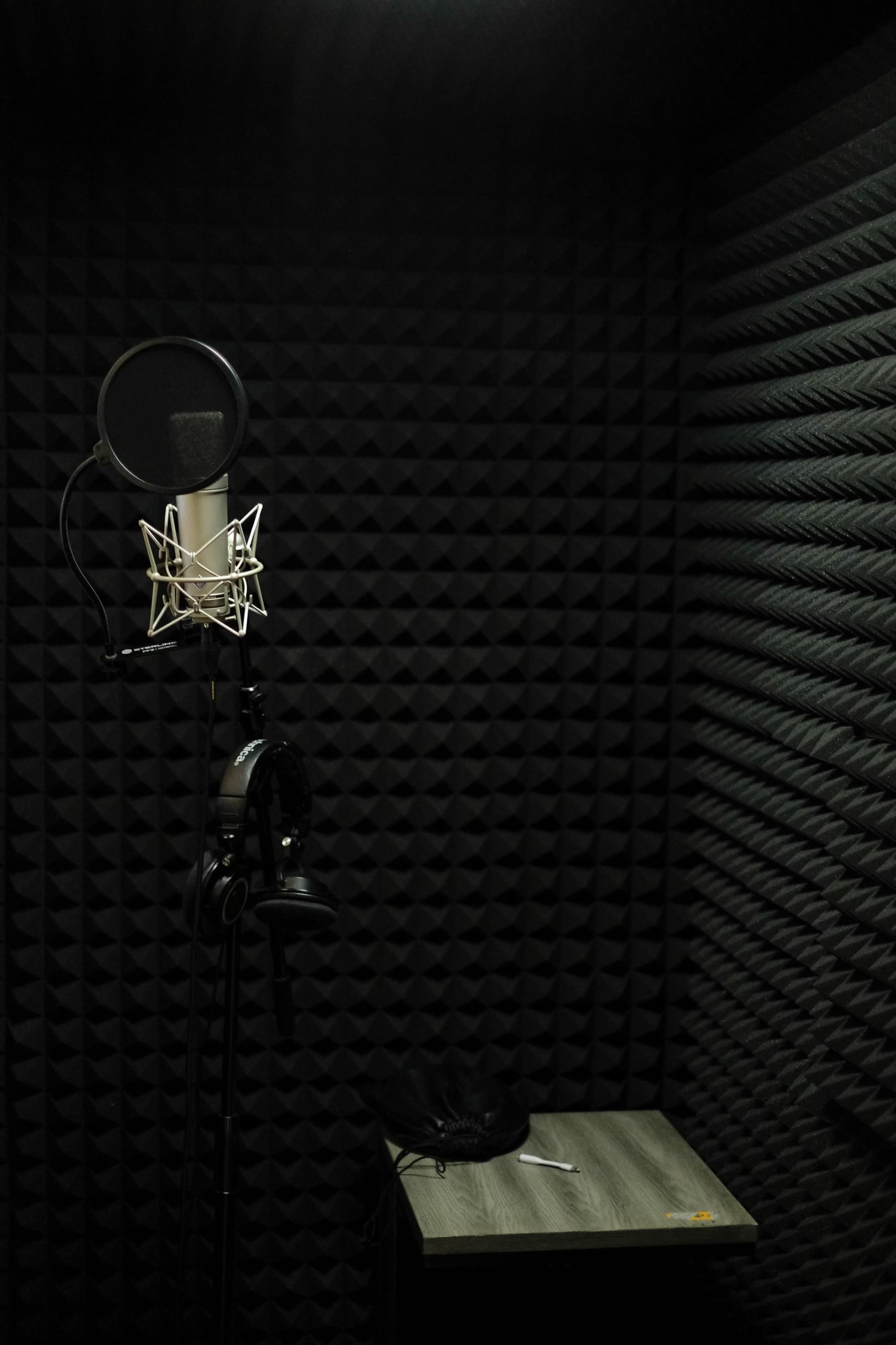 A soundproof recording booth with a microphone, headphones, and a small table against a wall covered in acoustic panels.