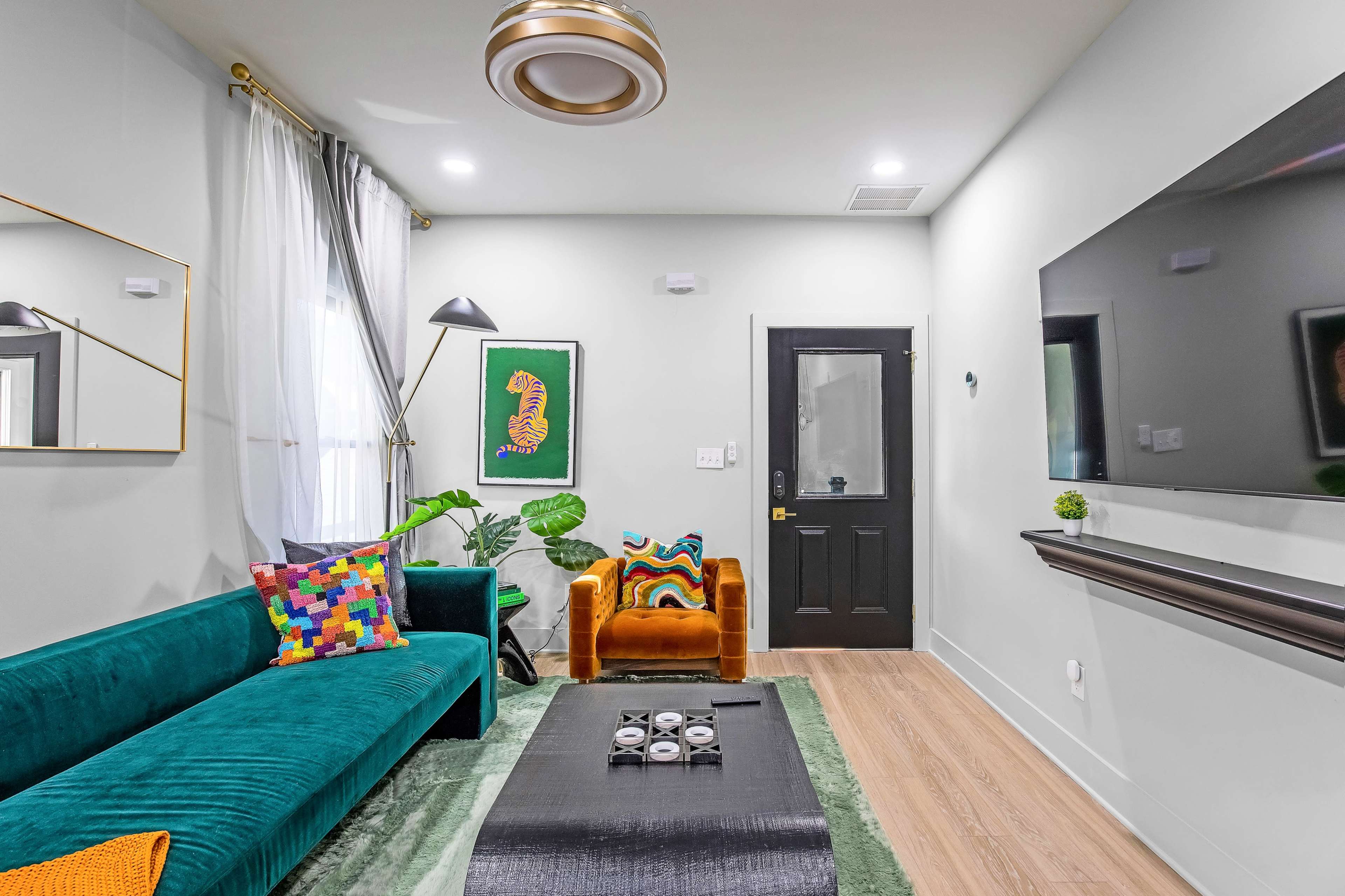 The living room features a teal sofa, an orange chair, a coffee table, and vibrant decor against light walls and wooden flooring.