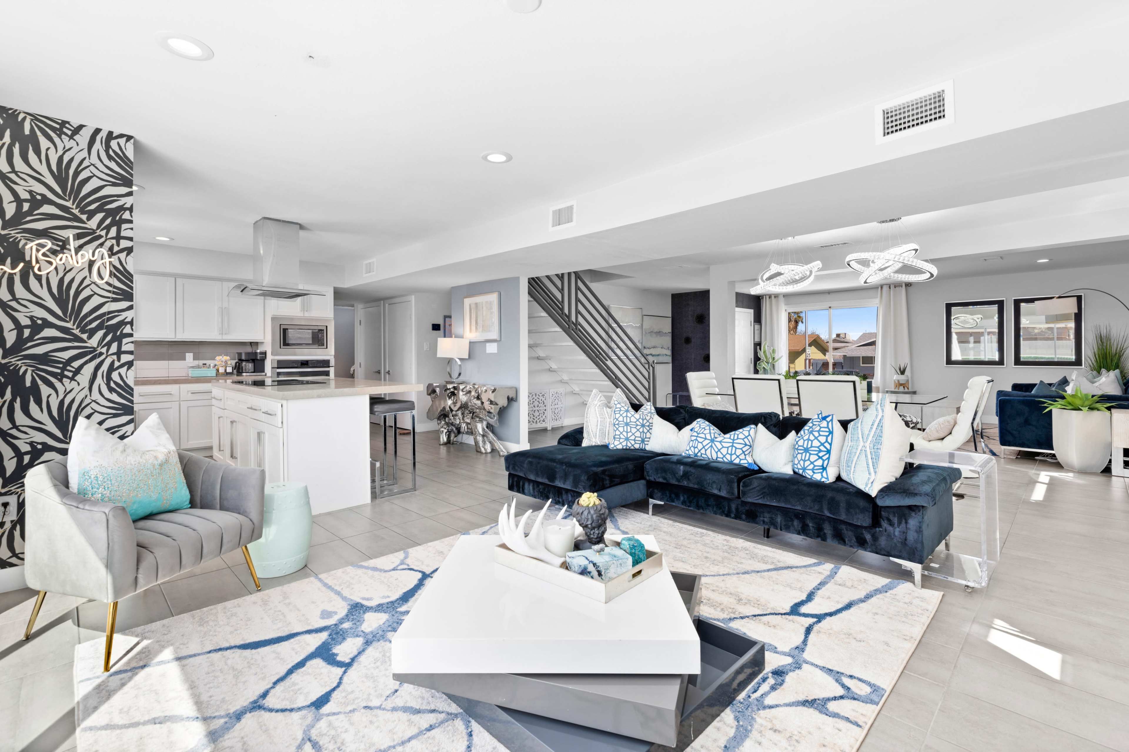 A modern living room with a blue sectional sofa, a coffee table, and a dining area, featuring light-colored tile flooring and stylish decor.