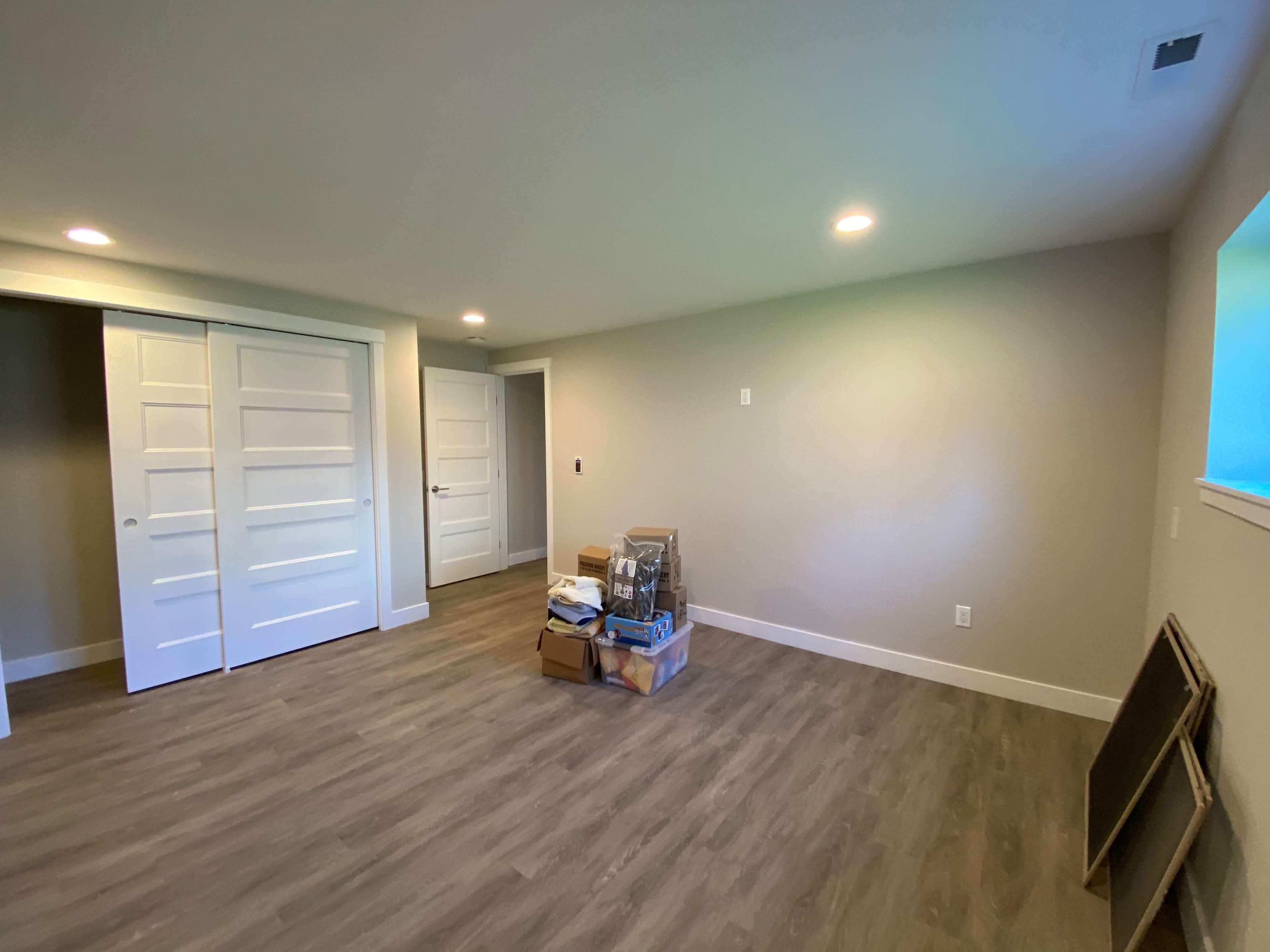 The image shows an empty room with light-colored walls, wooden flooring, and two white double doors on the left side.