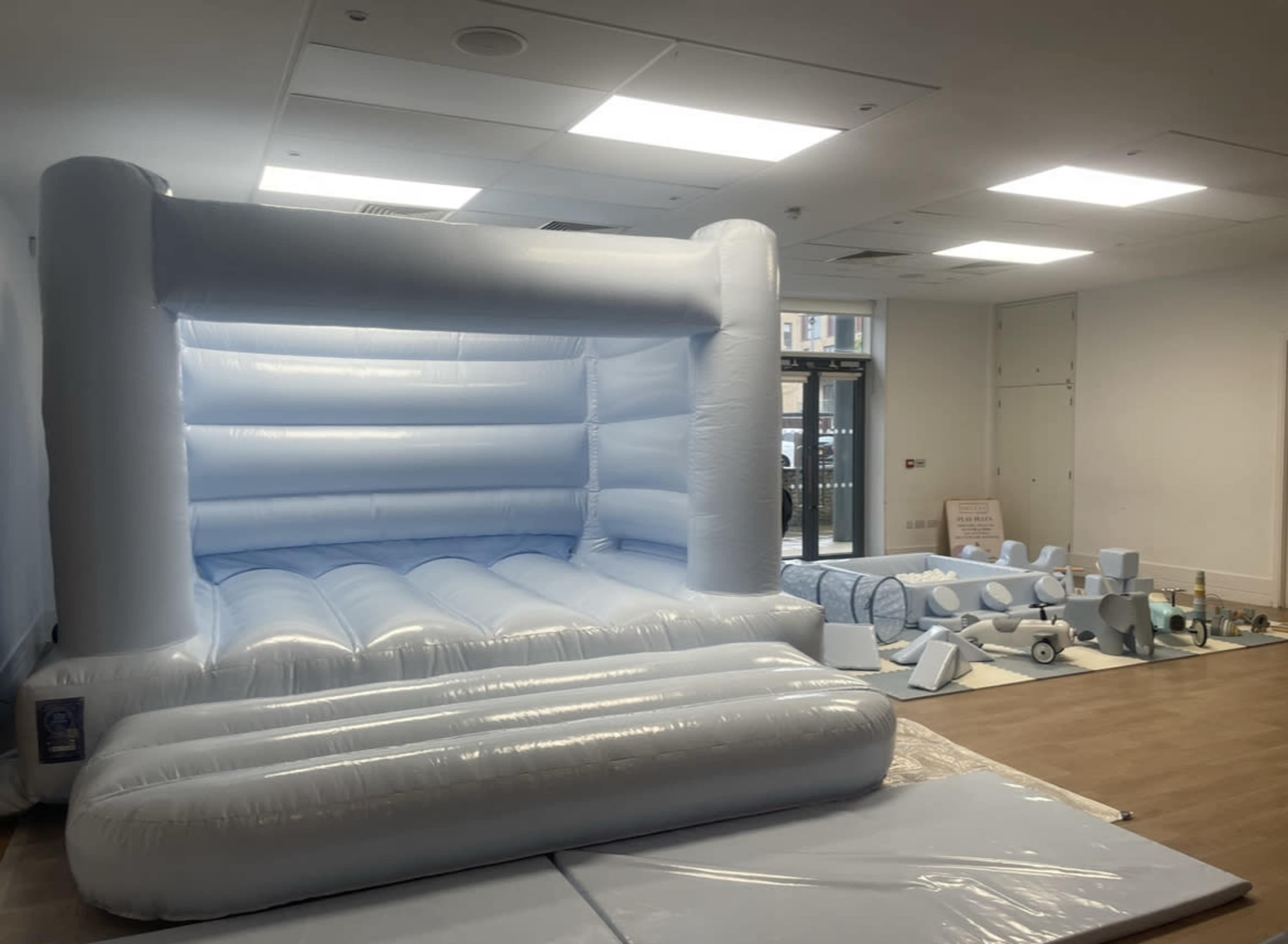 A large blue inflatable bouncy castle set up in a room, with various pieces of foam padding arranged nearby.