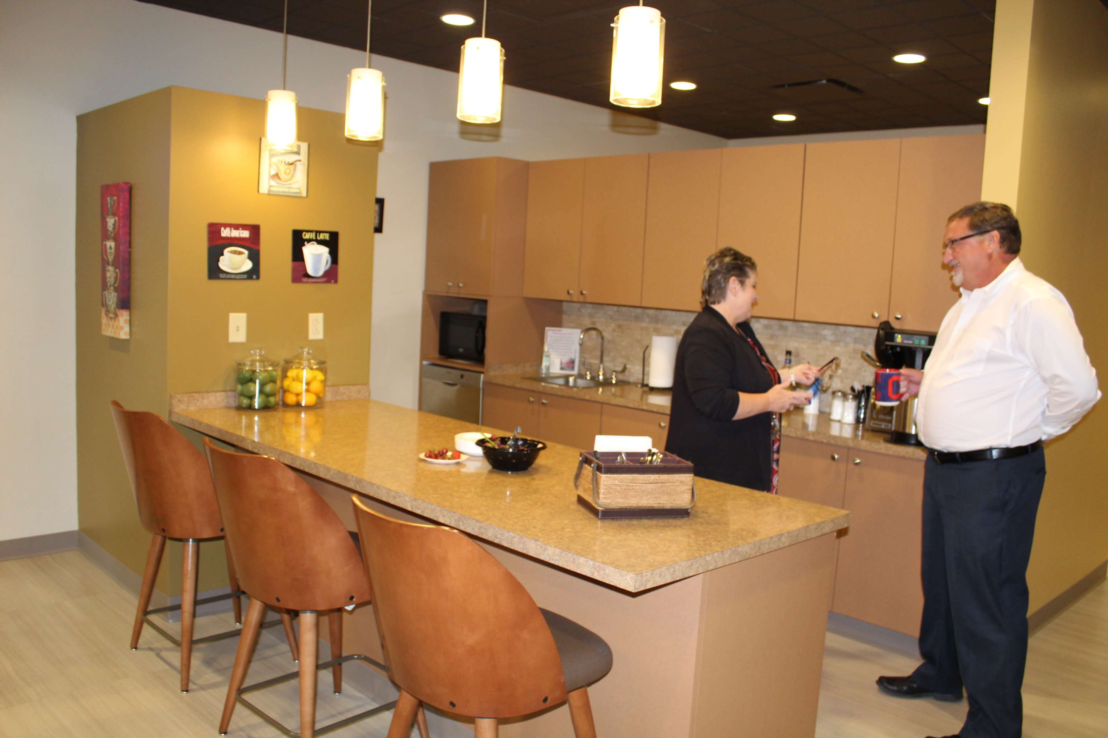 Two people are engaged in conversation in a modern kitchen area with a bar-style countertop and pendant lighting.