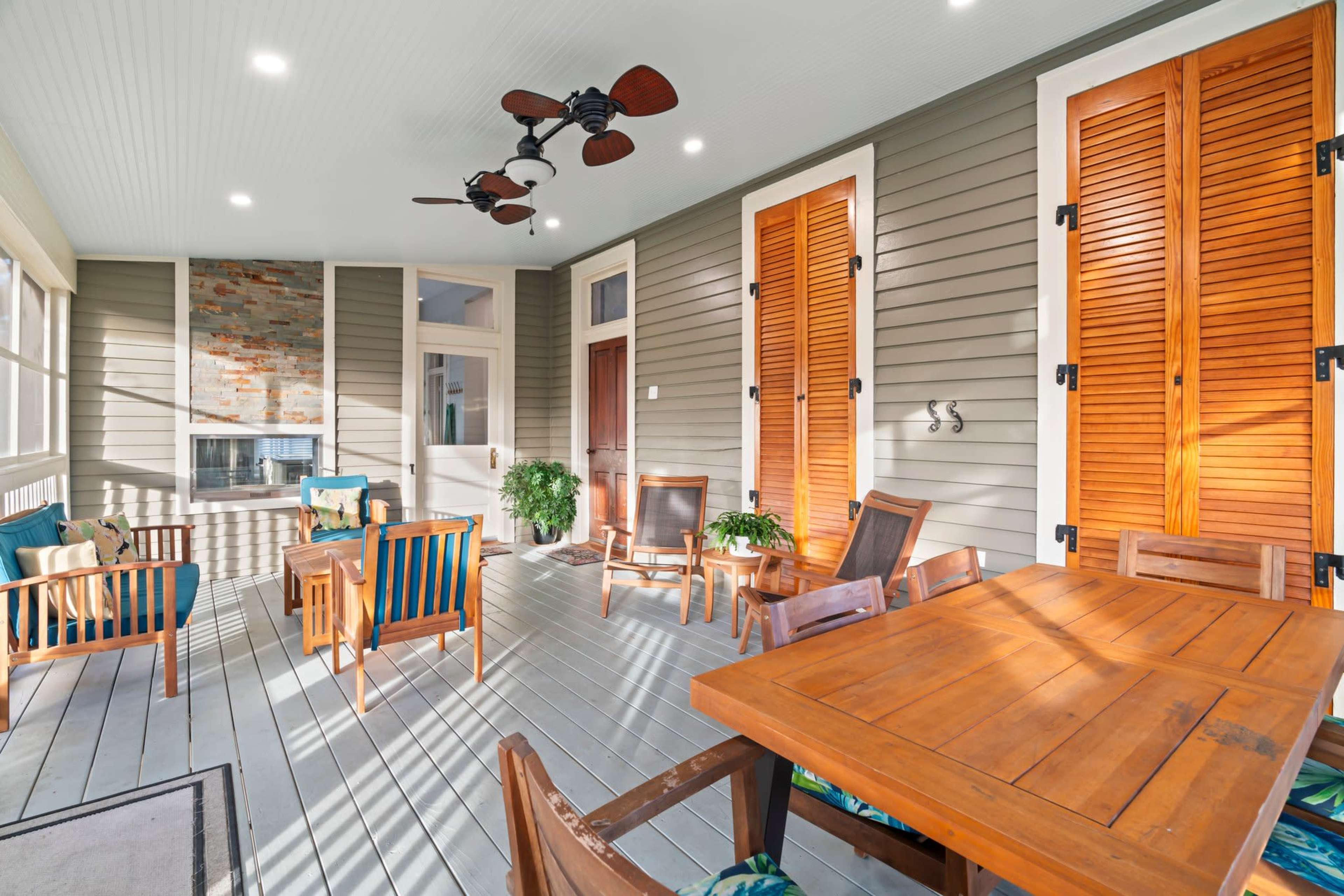 A spacious screened porch featuring wooden furniture, a ceiling fan, and decorative shuttered windows.