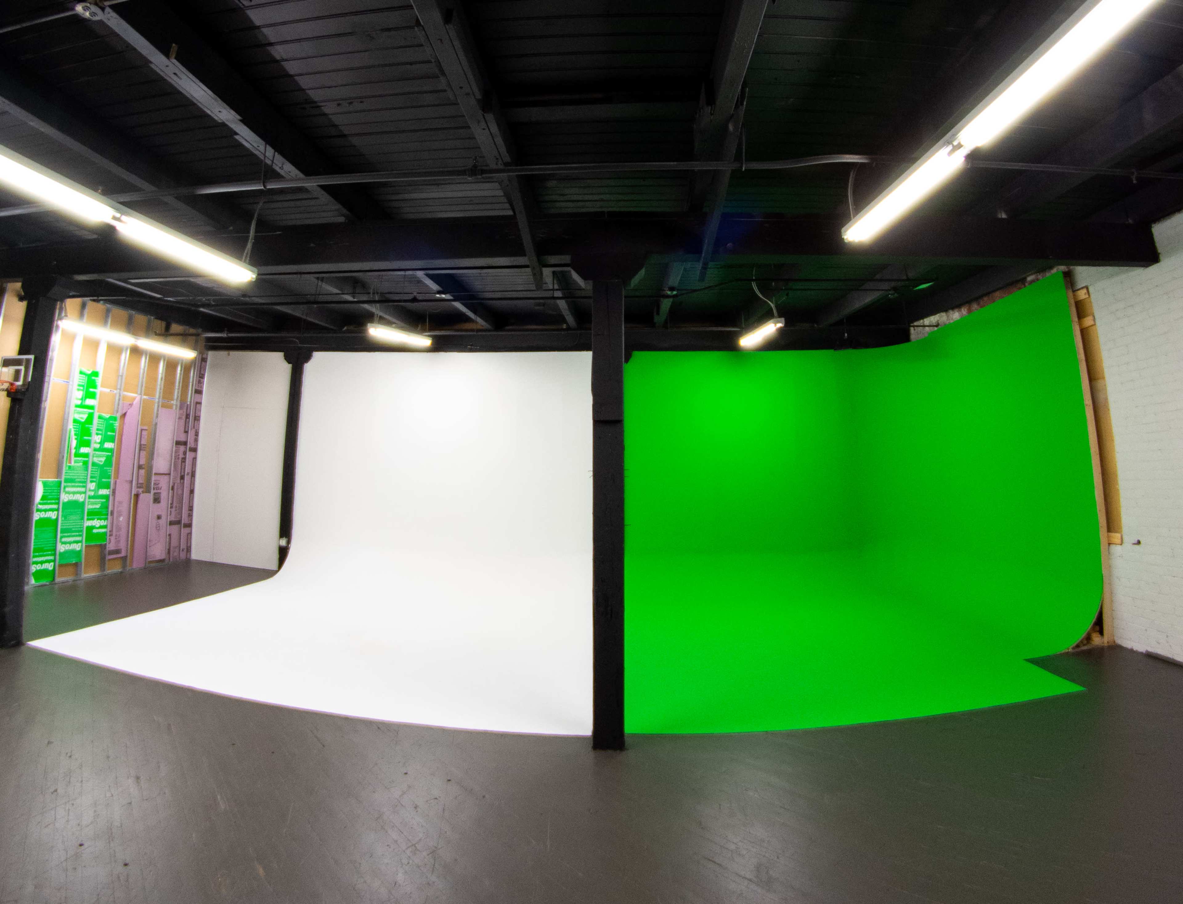 A studio space divided into two sections, one with a white backdrop and the other with a green backdrop, both set on a dark floor.
