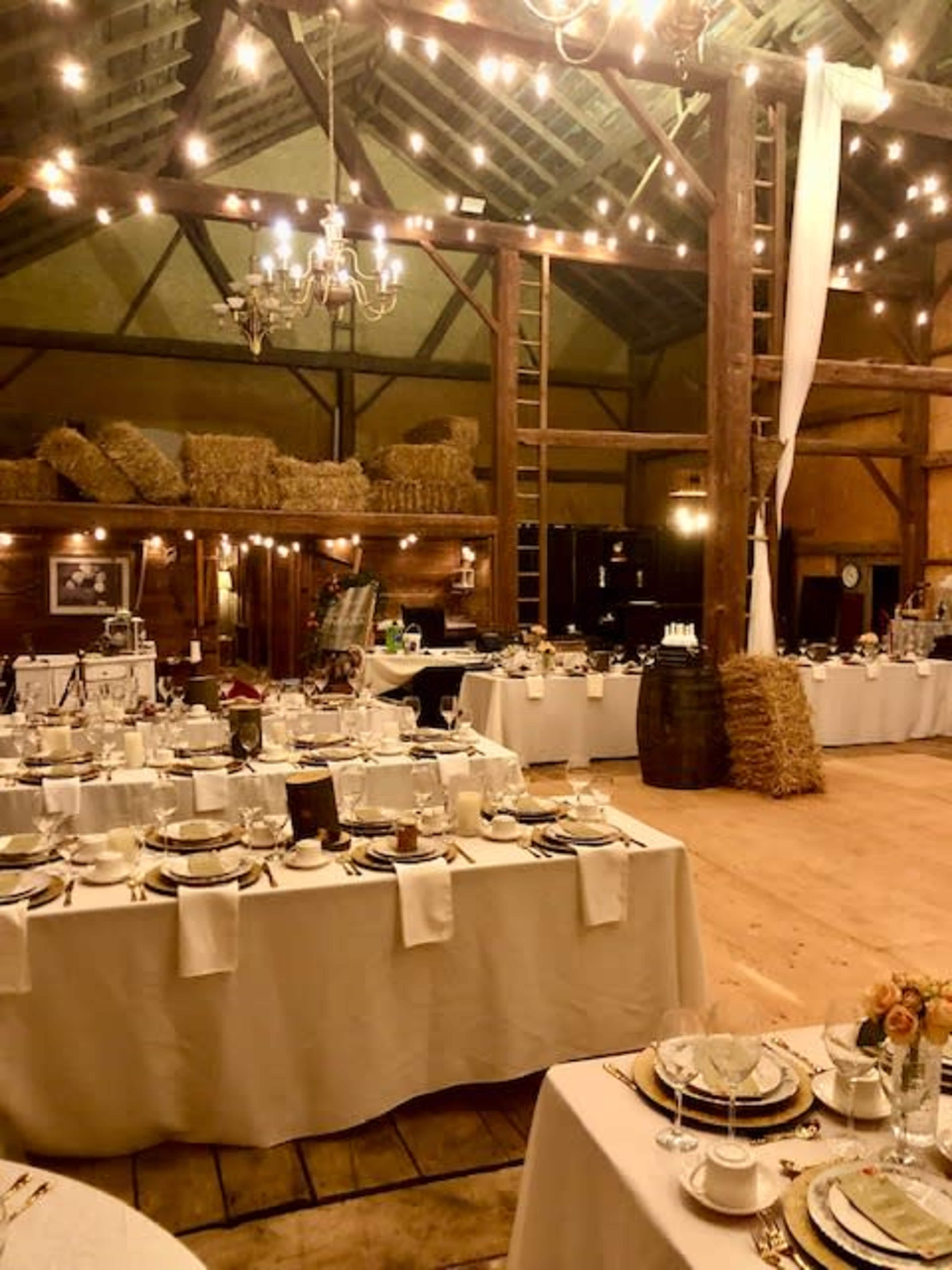 A rustic banquet hall with elegantly set tables, string lights, and wooden beams.