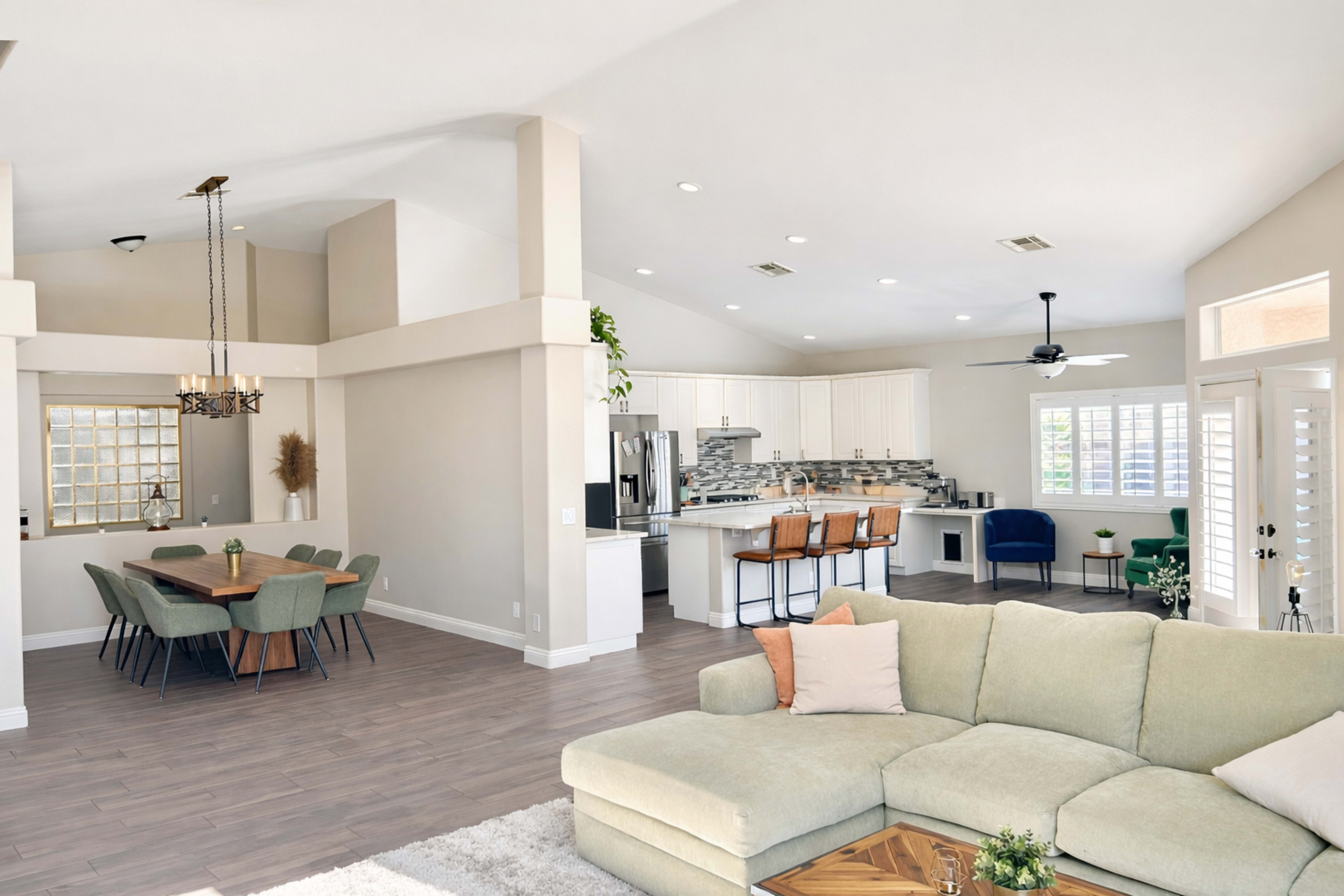 The image shows an open-concept living space with a modern kitchen, dining area, and a comfortable seating area featuring a large sectional sofa.