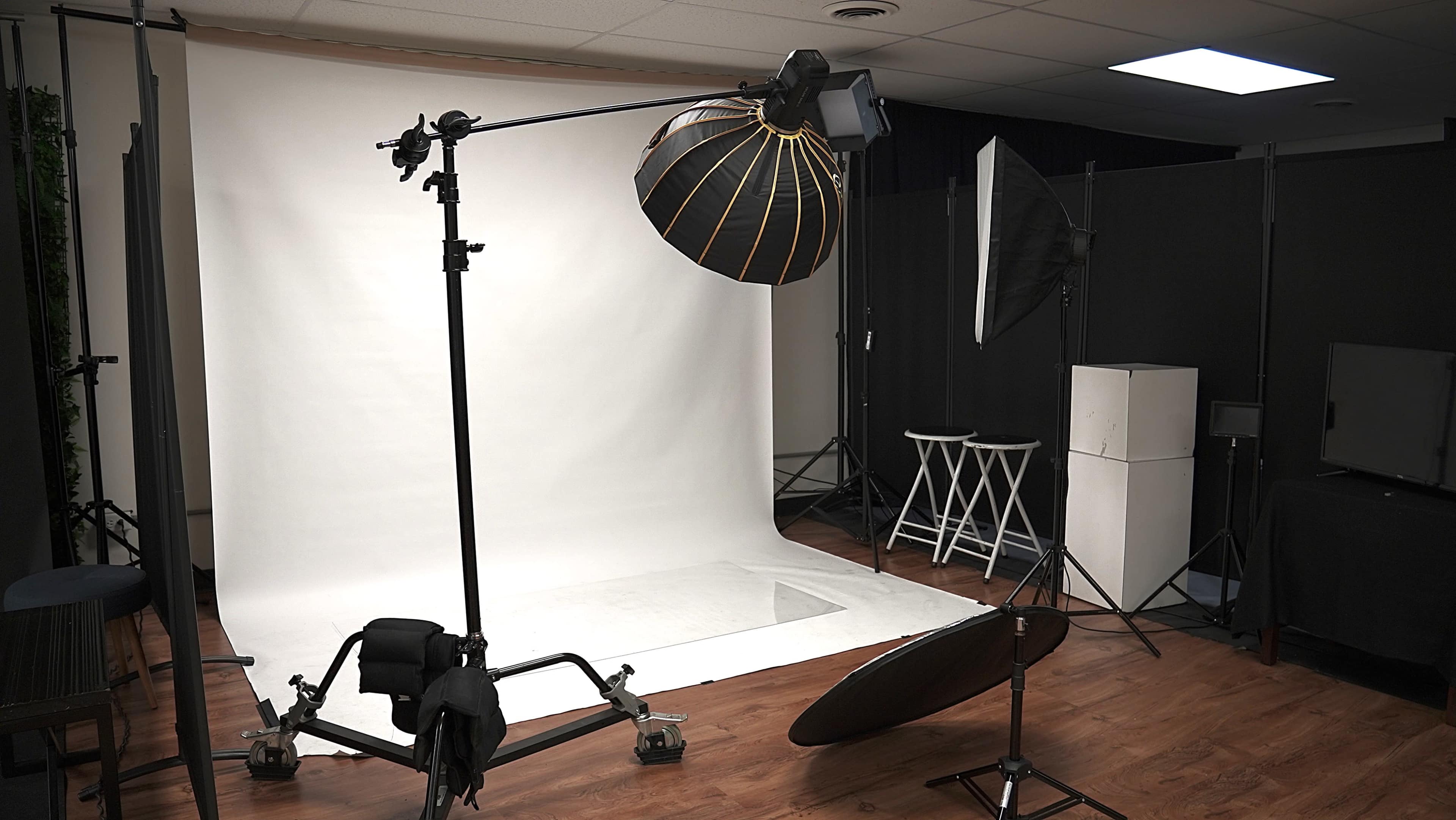 The image shows a photography studio setup with a large softbox, a reflector, and a roll of white backdrop.
