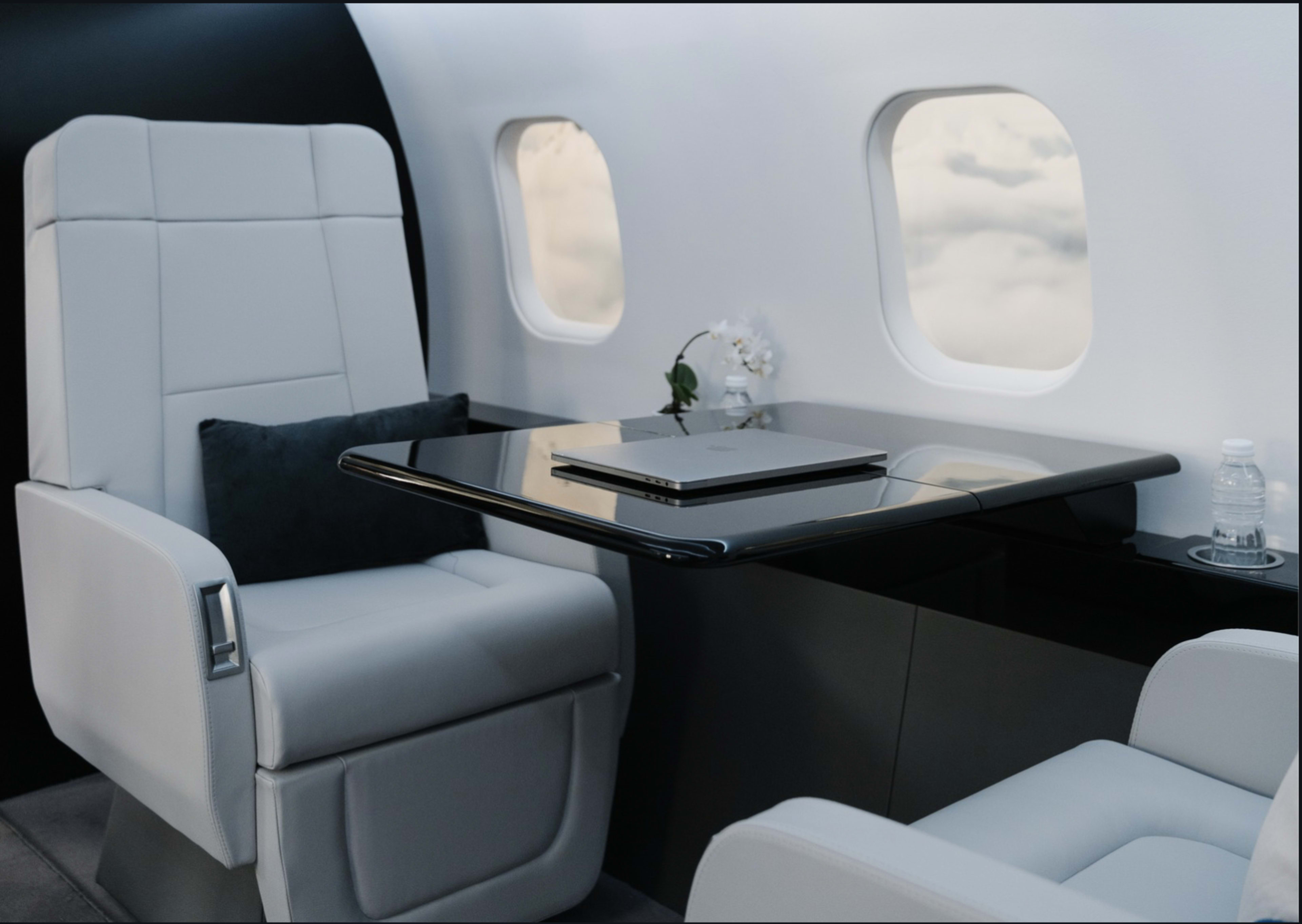 The image shows a luxurious interior of a private jet with two leather chairs and a polished table featuring a laptop and a small vase with a flower.