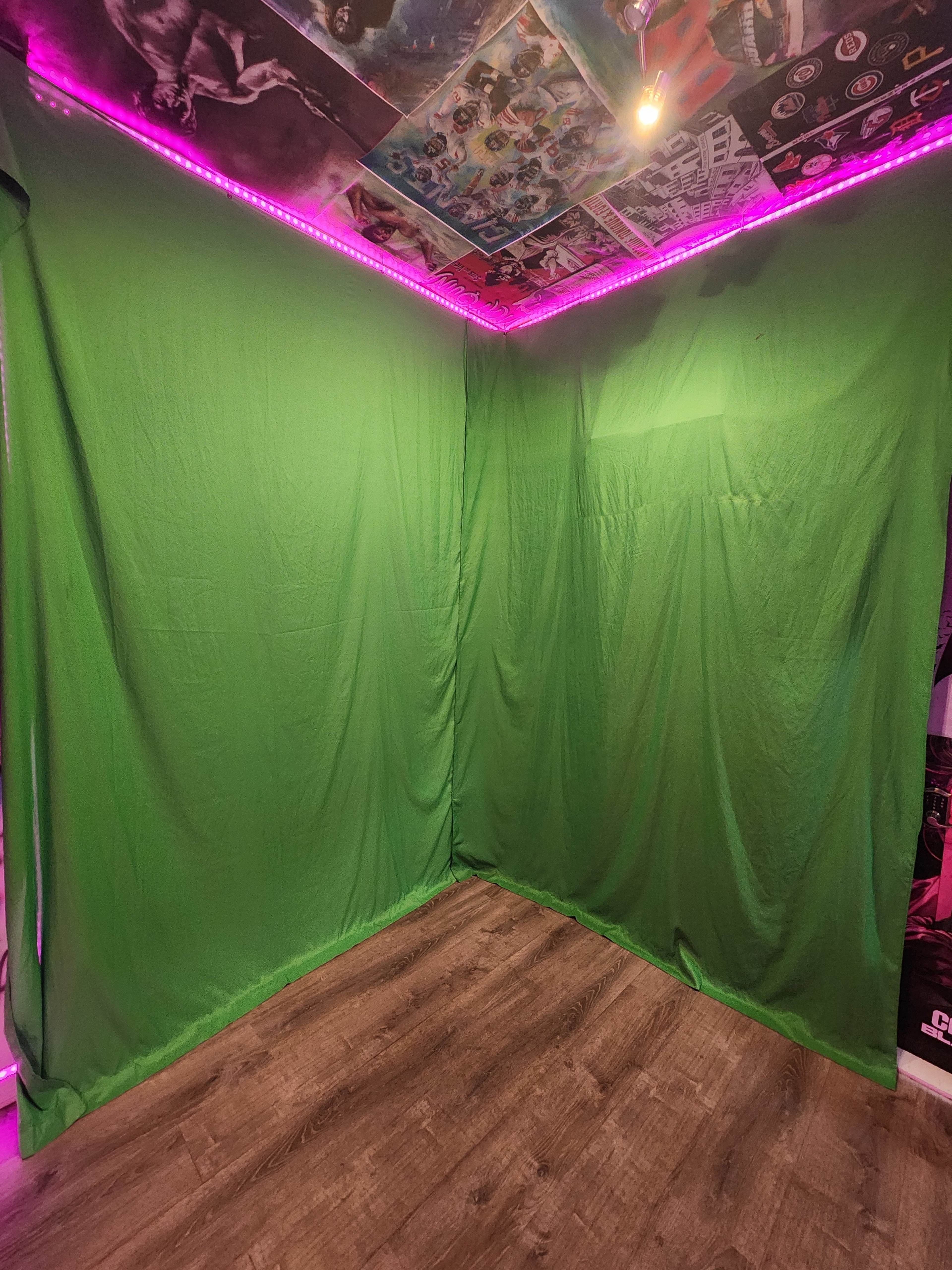 The image shows a corner of a room draped in a green fabric, with colorful posters on the ceiling and pink LED lights illuminating the space.