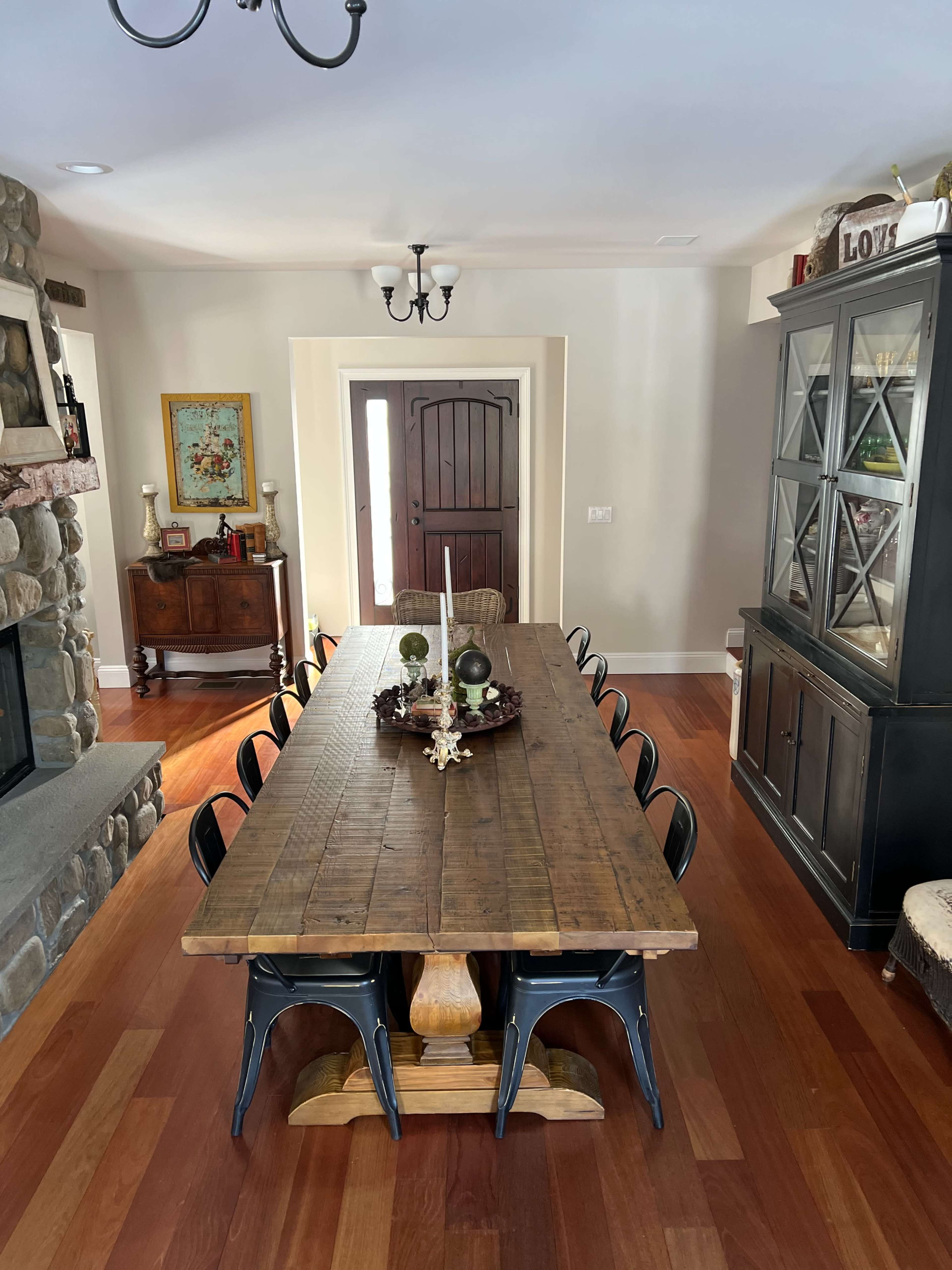 A long wooden dining table with black chairs is set in a room featuring a stone fireplace, a large cabinet, and a decorative wooden door.