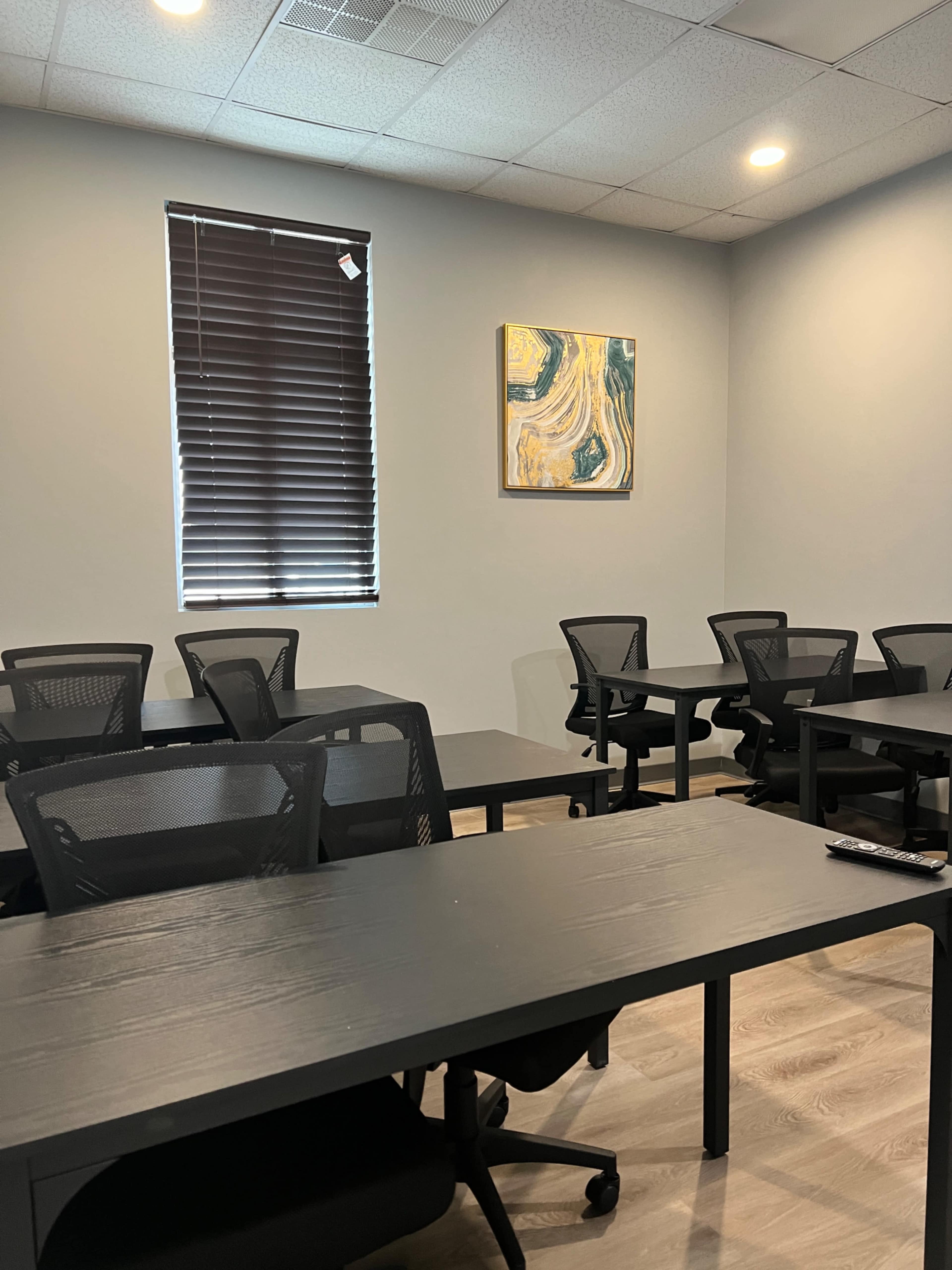 A classroom features several black tables and chairs arranged neatly, with a large abstract painting hanging on the wall.