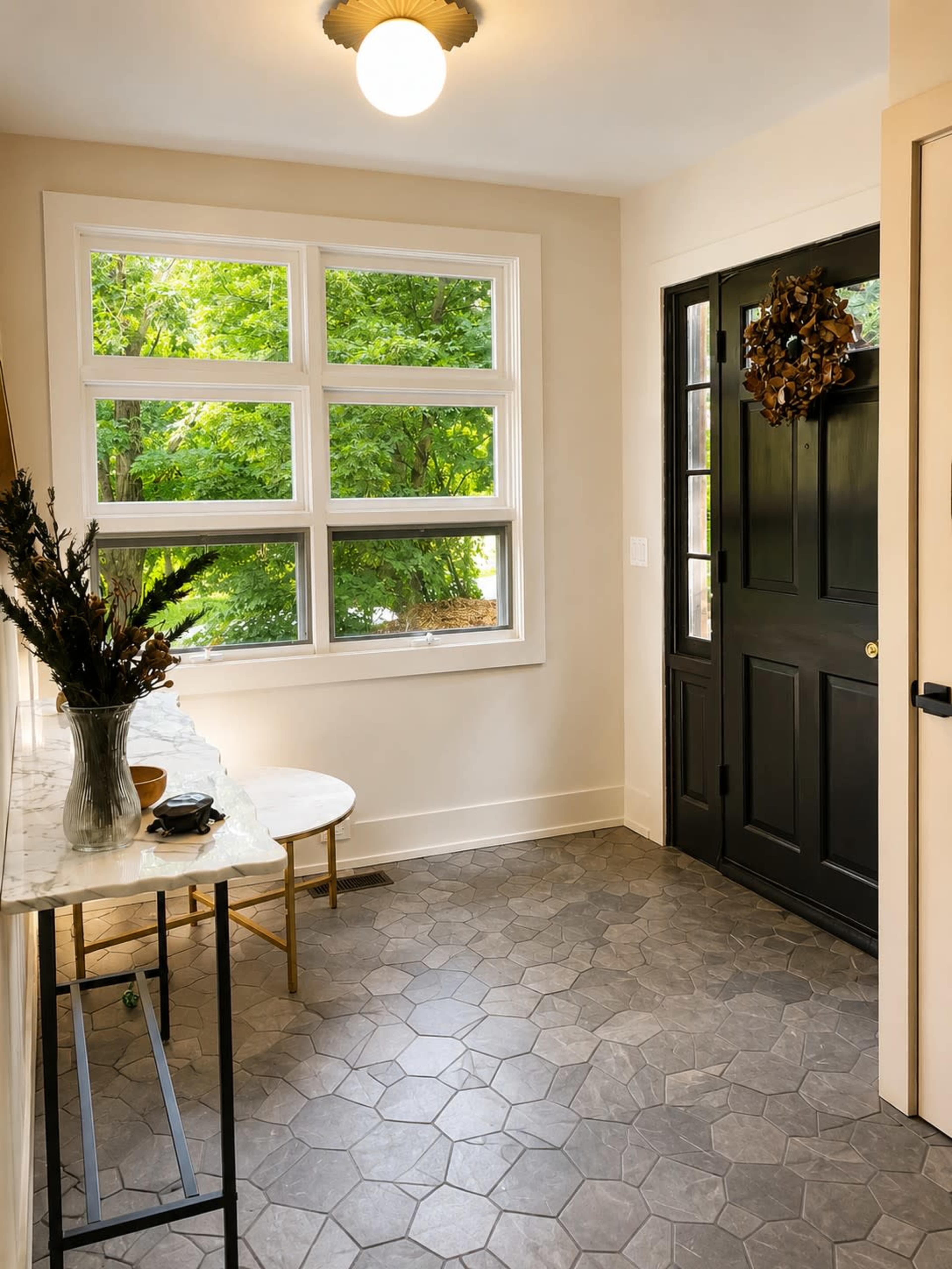 The image depicts a bright entryway with a black front door, a small round table, and large windows allowing natural light to illuminate the space.