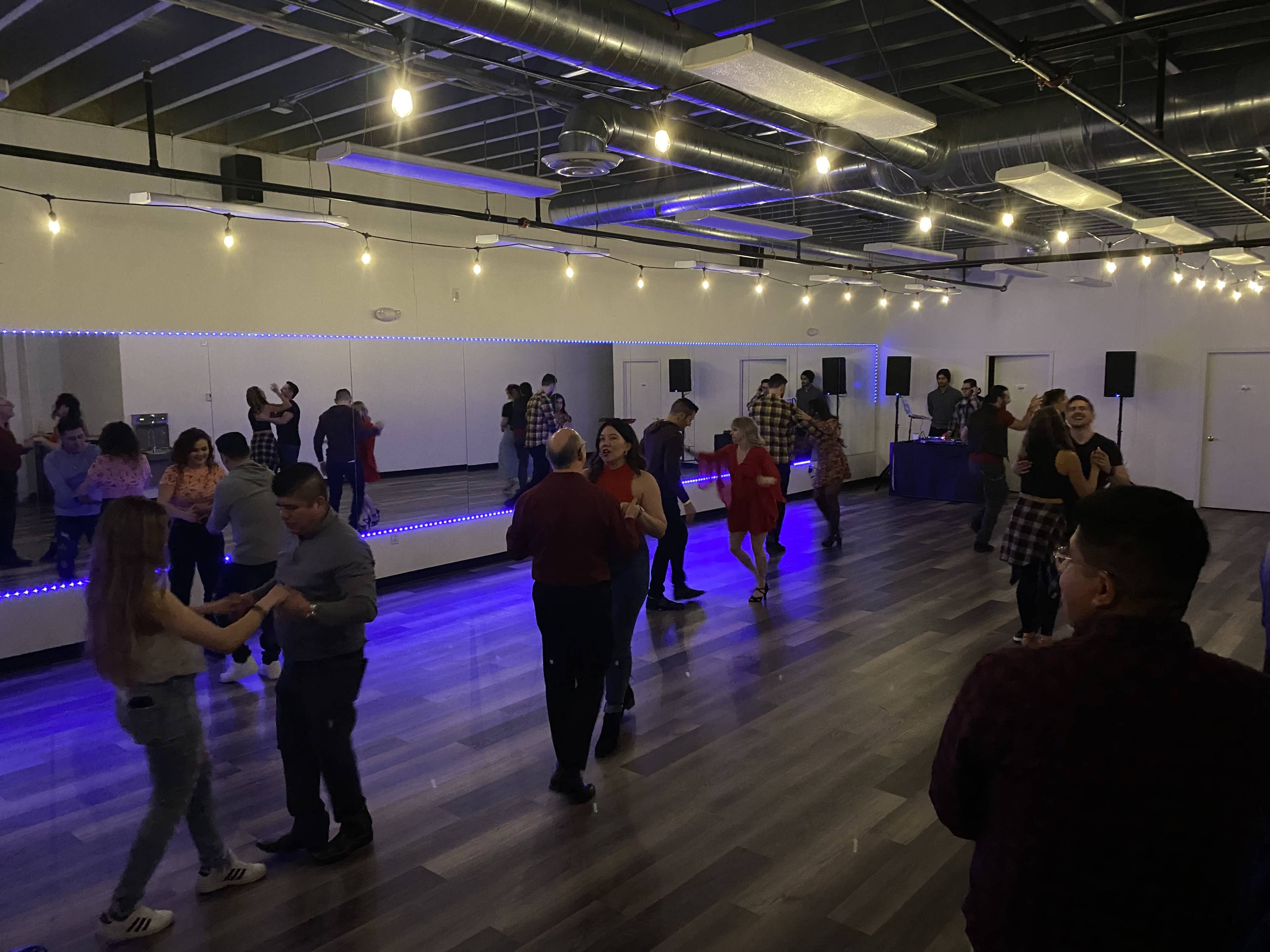 A lively dance event takes place in a spacious room with mirrored walls and colorful lights.