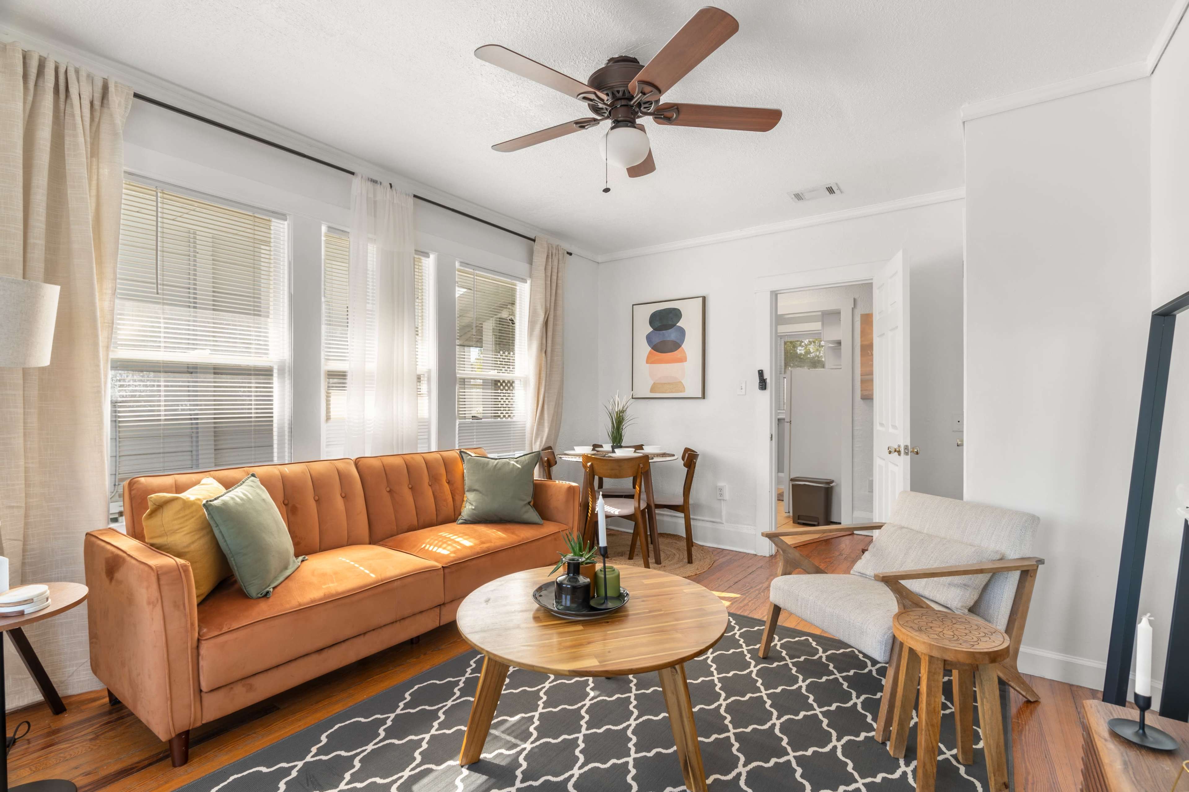 A cozy living room featuring an orange couch, a round wooden coffee table, and a small dining area with a table and chairs.