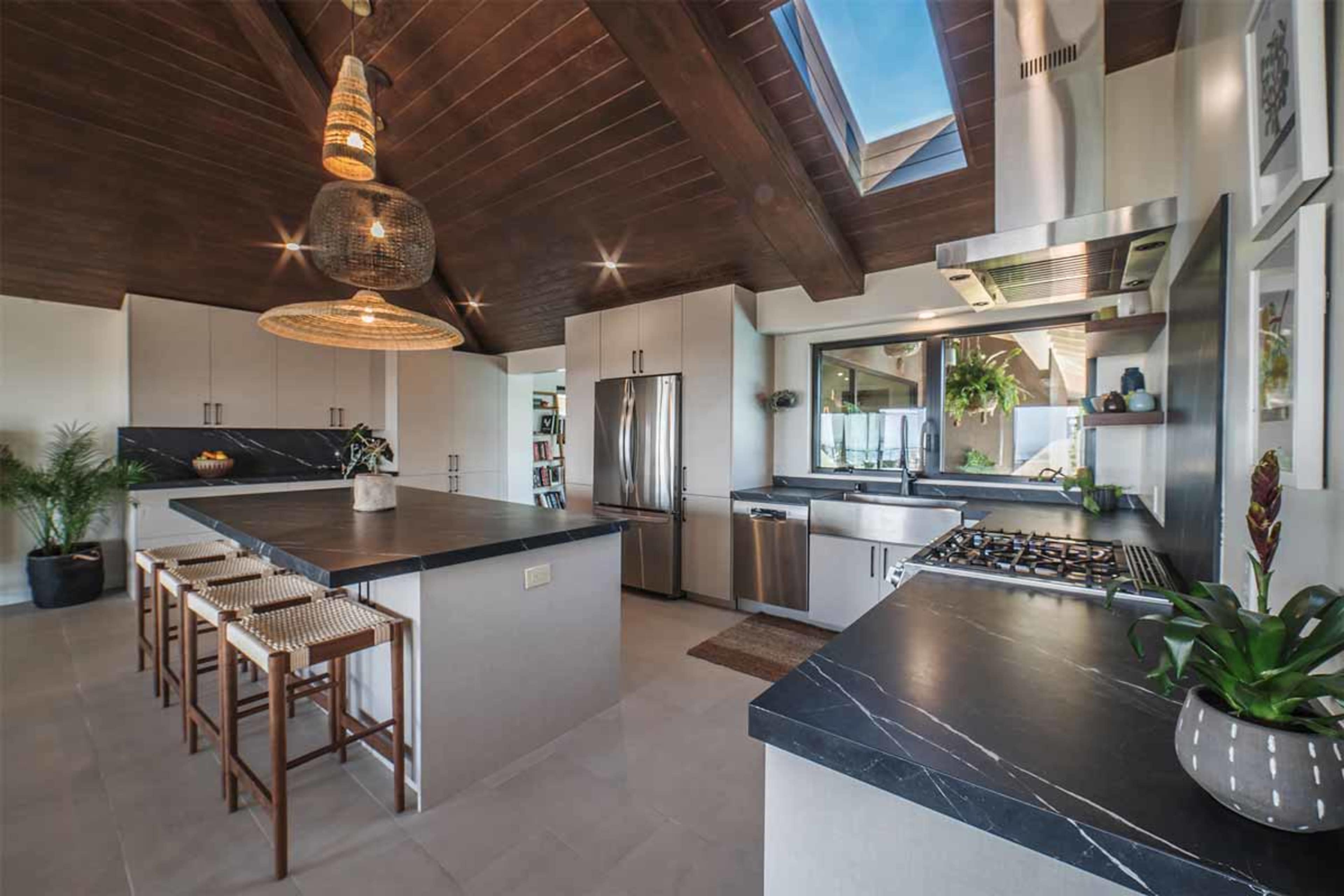 A modern kitchen with open shelving, a large dark countertop island, woven pendant lights, and stainless steel appliances.