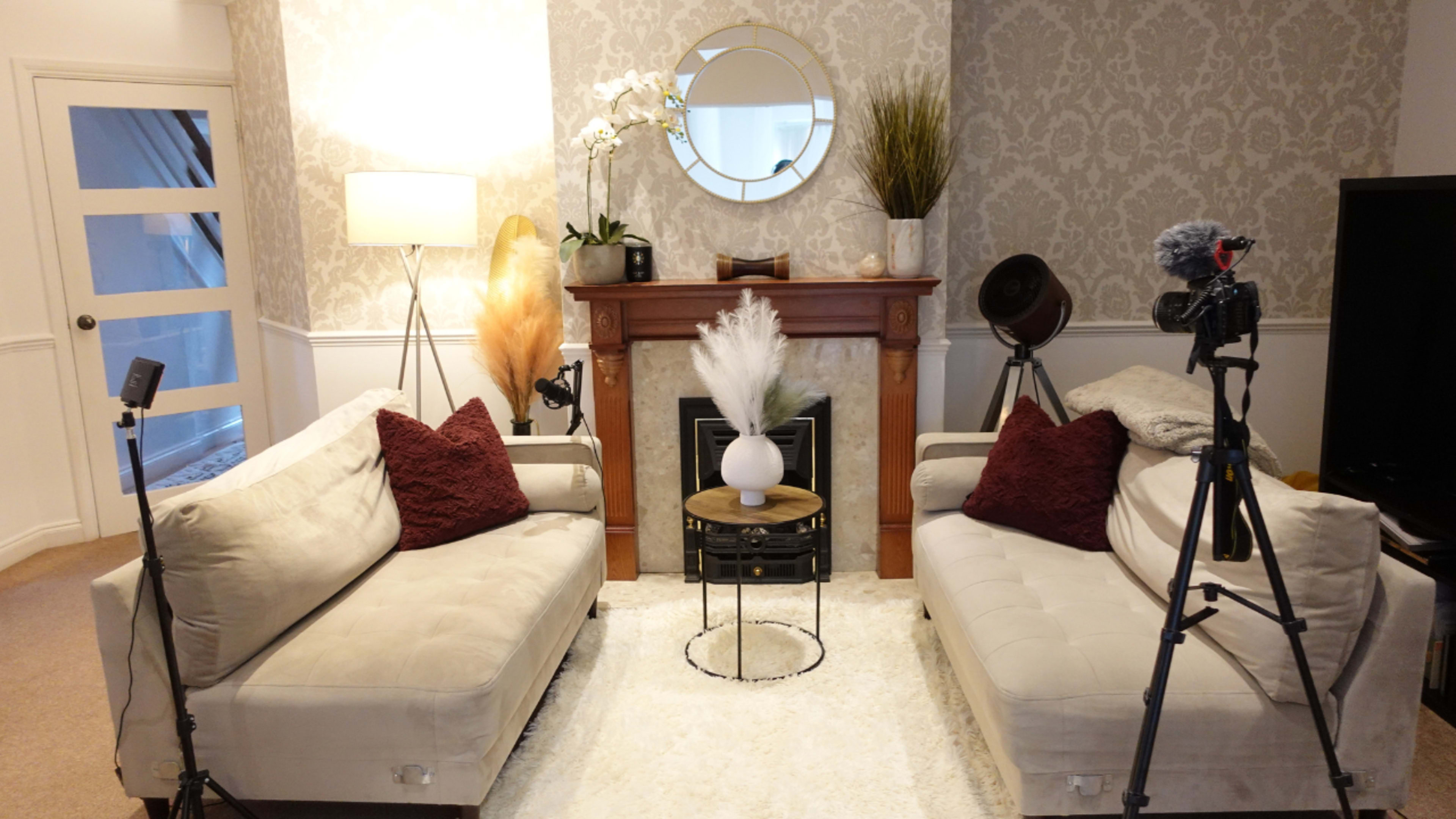 A cozy living room features two sofas facing a coffee table, surrounded by decorative plants and media equipment.