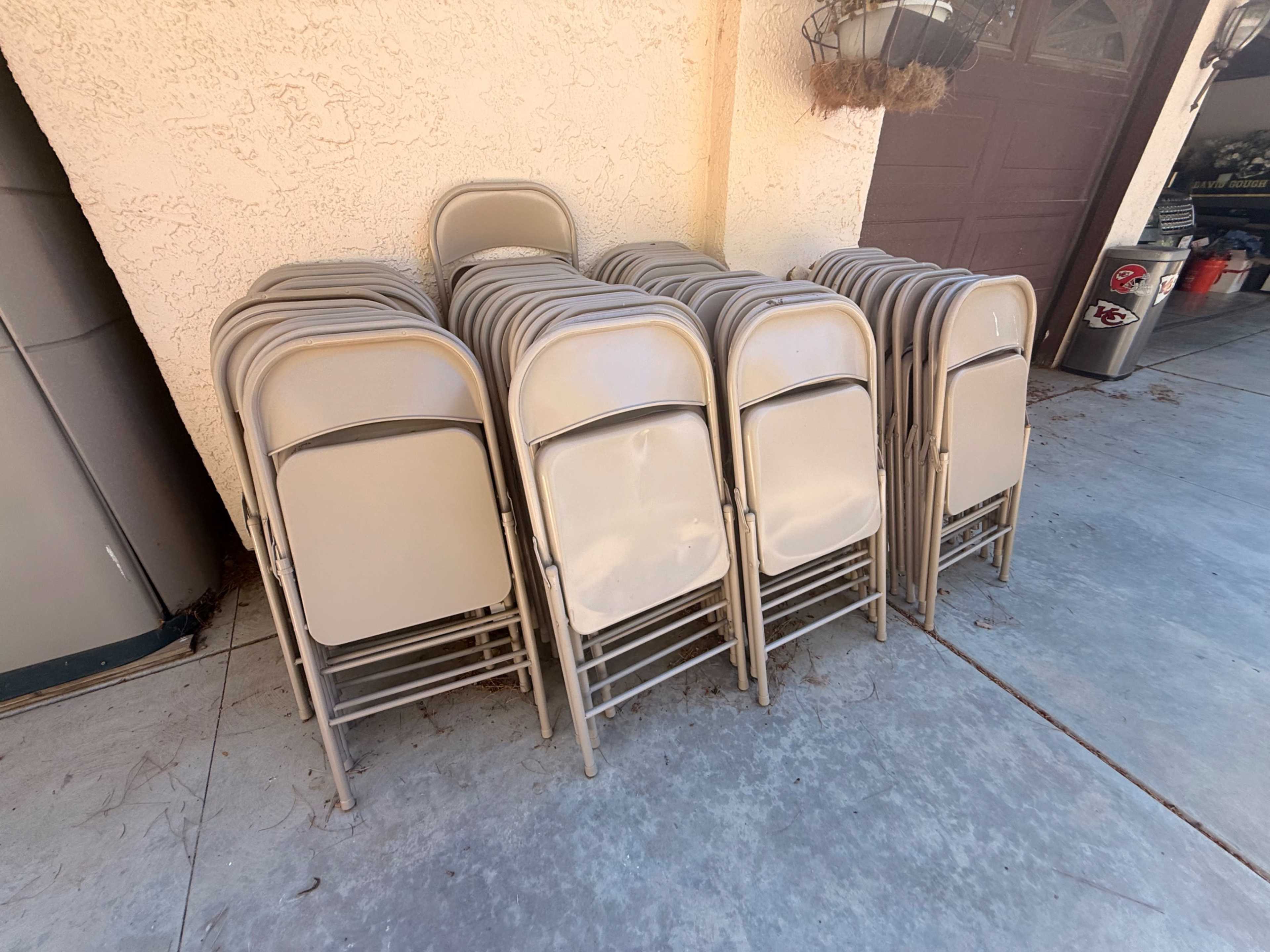 A stack of several beige folding chairs is positioned against a wall in a garage.