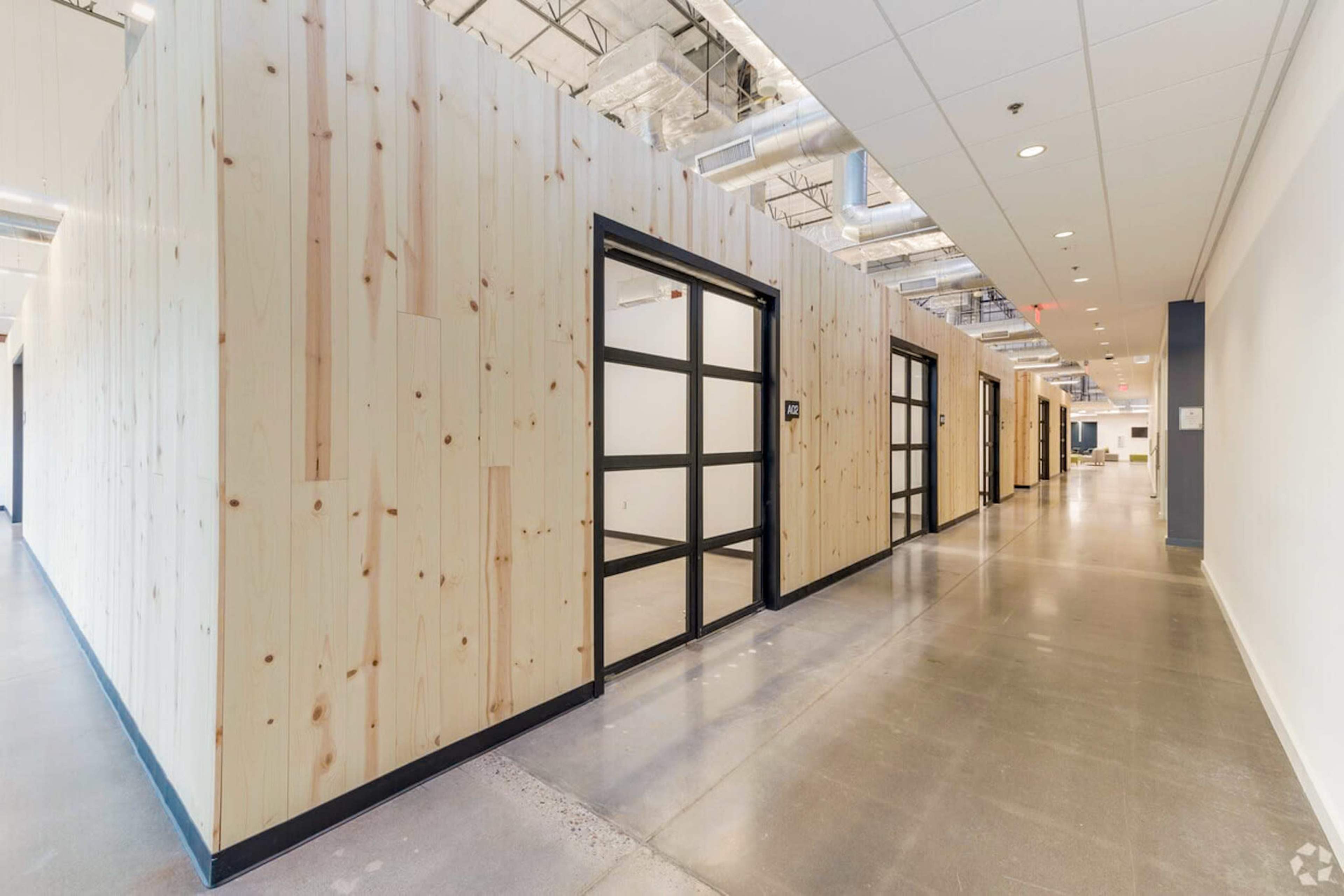 The image shows a modern hallway lined with wooden-paneled walls and several glass-fronted office doors.