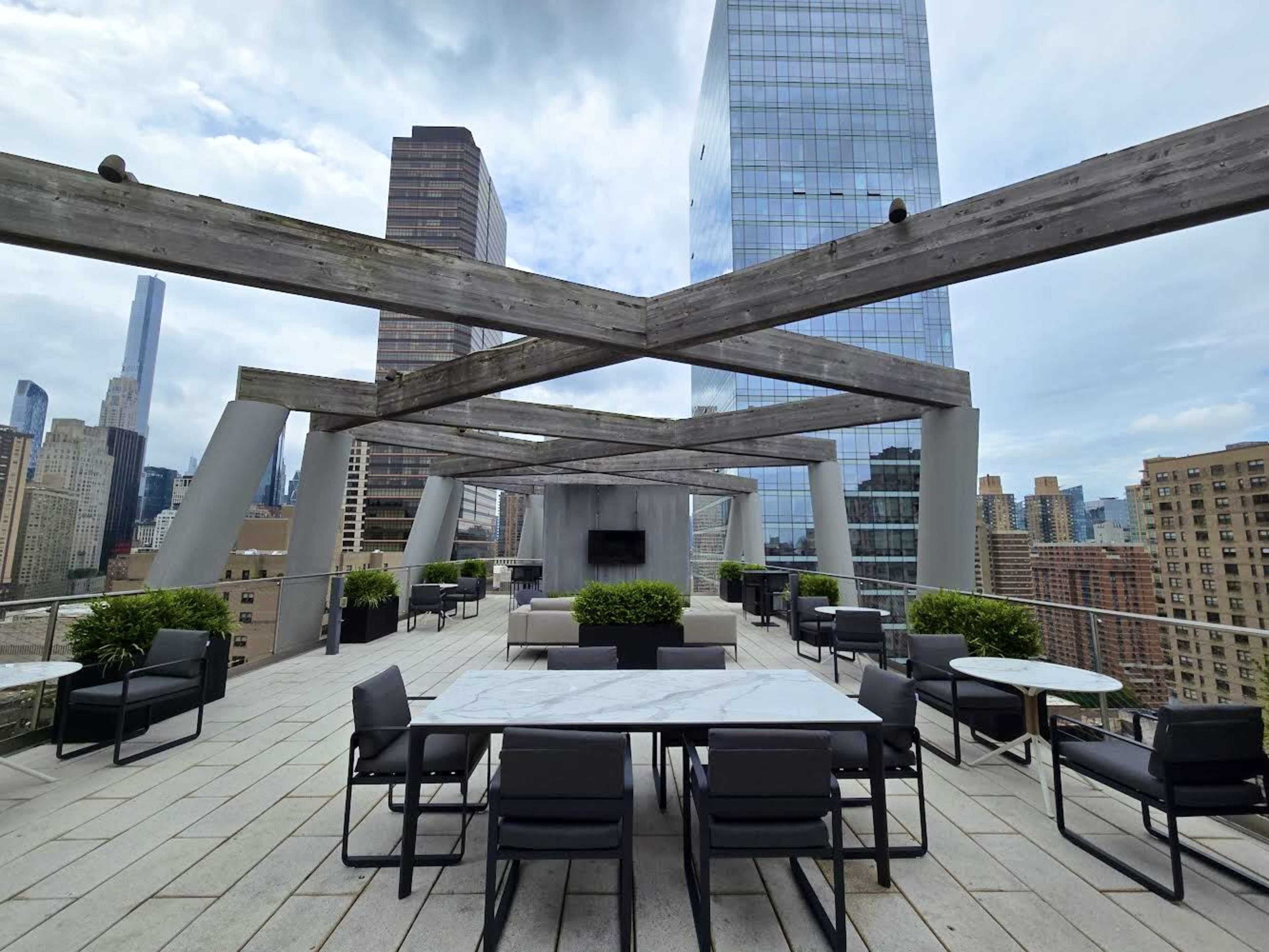 A rooftop terrace with tables and chairs, surrounded by modern skyscrapers under an overcast sky.