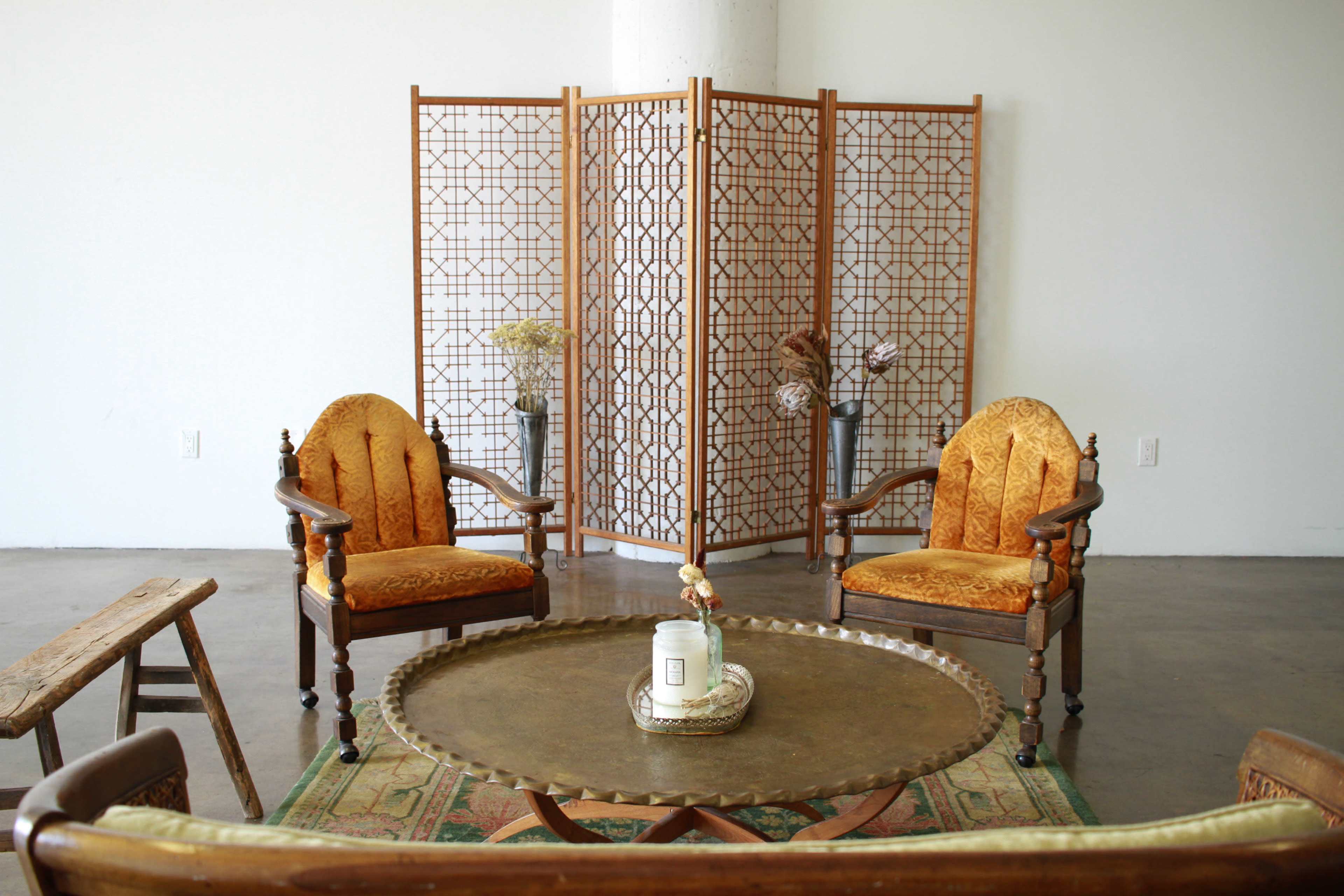 A seating area with two vintage chairs, a round coffee table, and a folding screen in a minimalistic room.