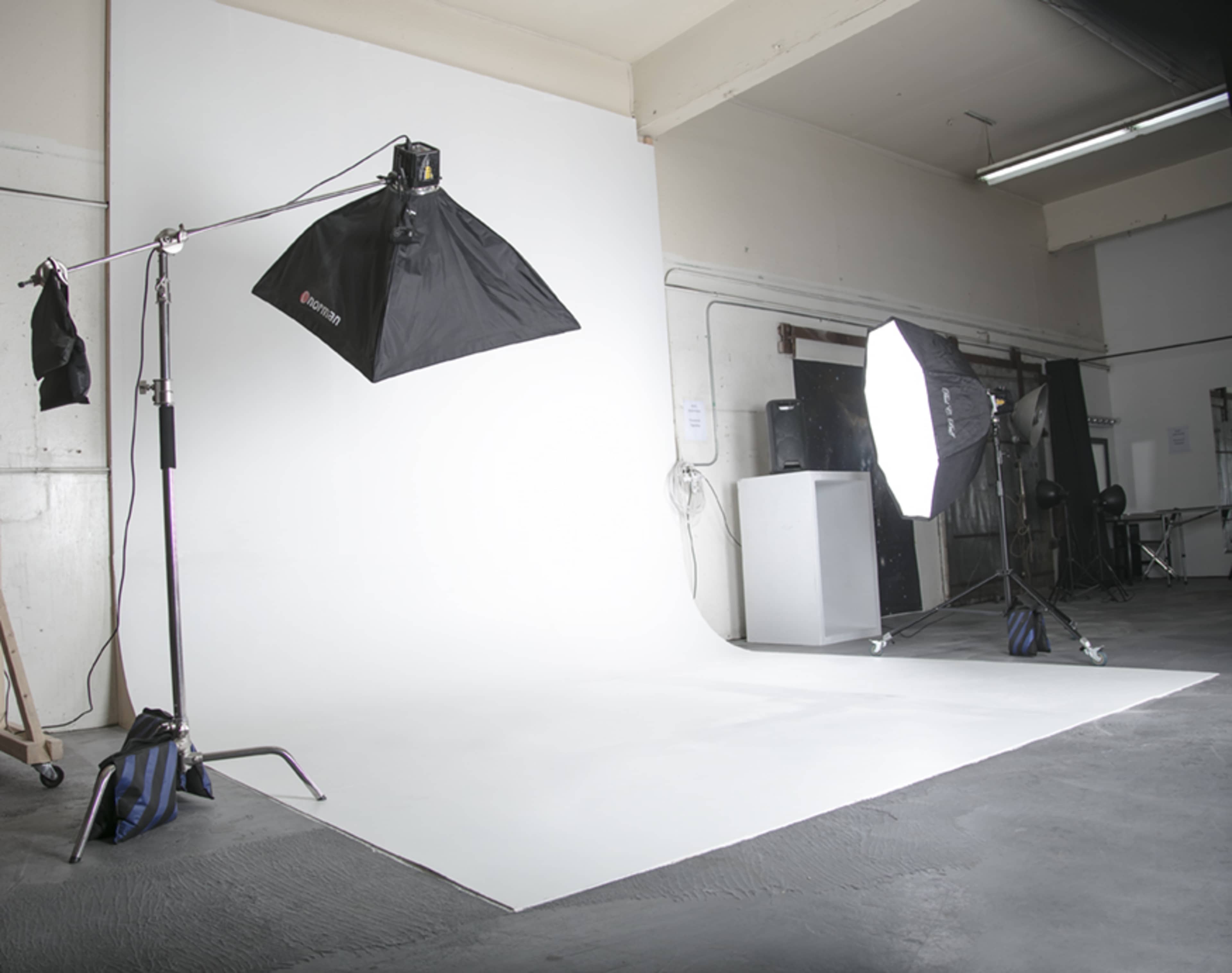 The image shows a photography studio with a seamless white backdrop and lighting equipment set up on both sides.