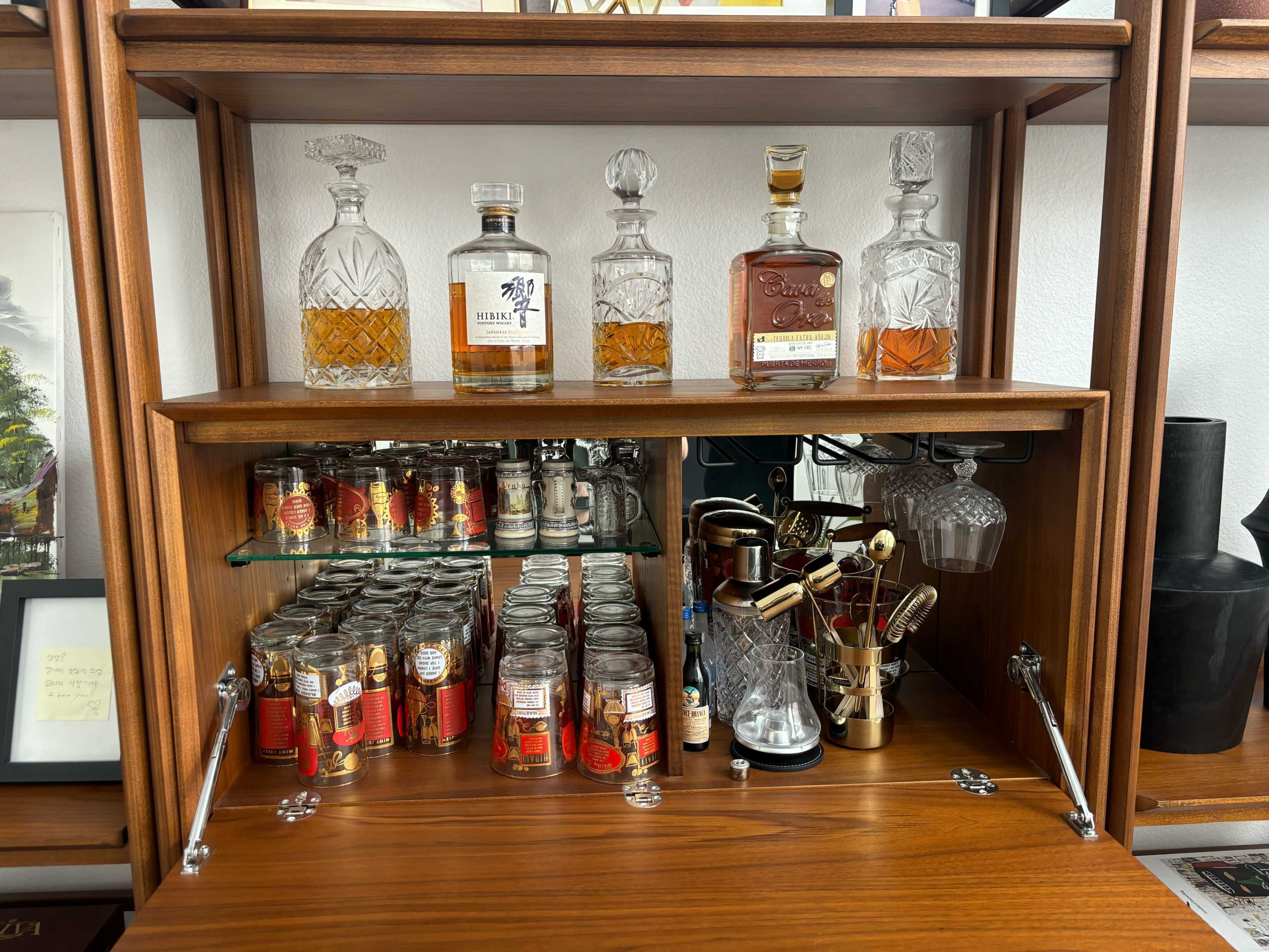 A wooden shelf displays a selection of glass decanters and jars filled with various spirits and ingredients for crafting cocktails.