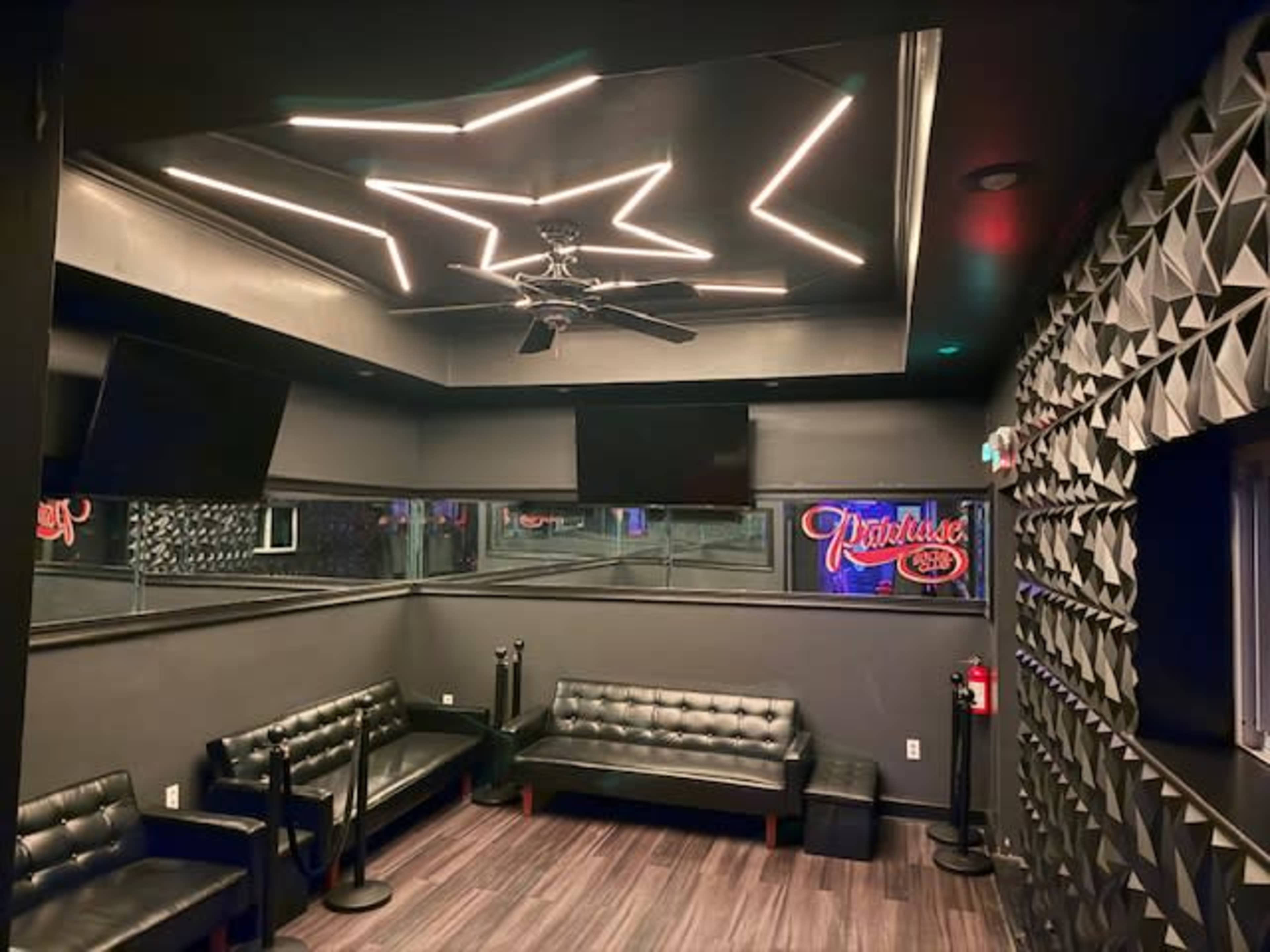 The image shows a modern interior of a small, private room with black walls, a sleek ceiling, and comfortable black seating.