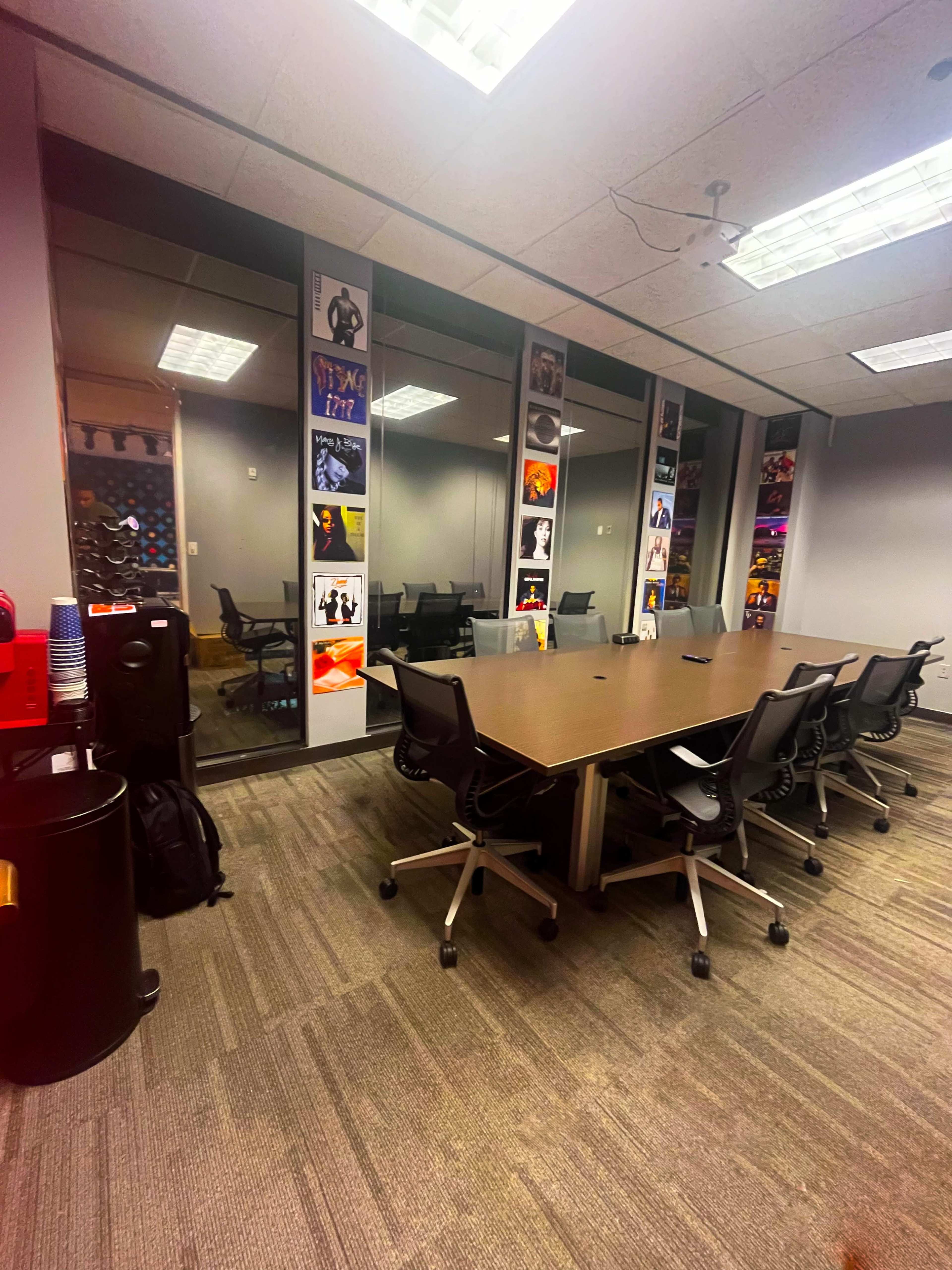 A modern conference room with a large table surrounded by chairs, featuring glass walls adorned with colorful posters.
