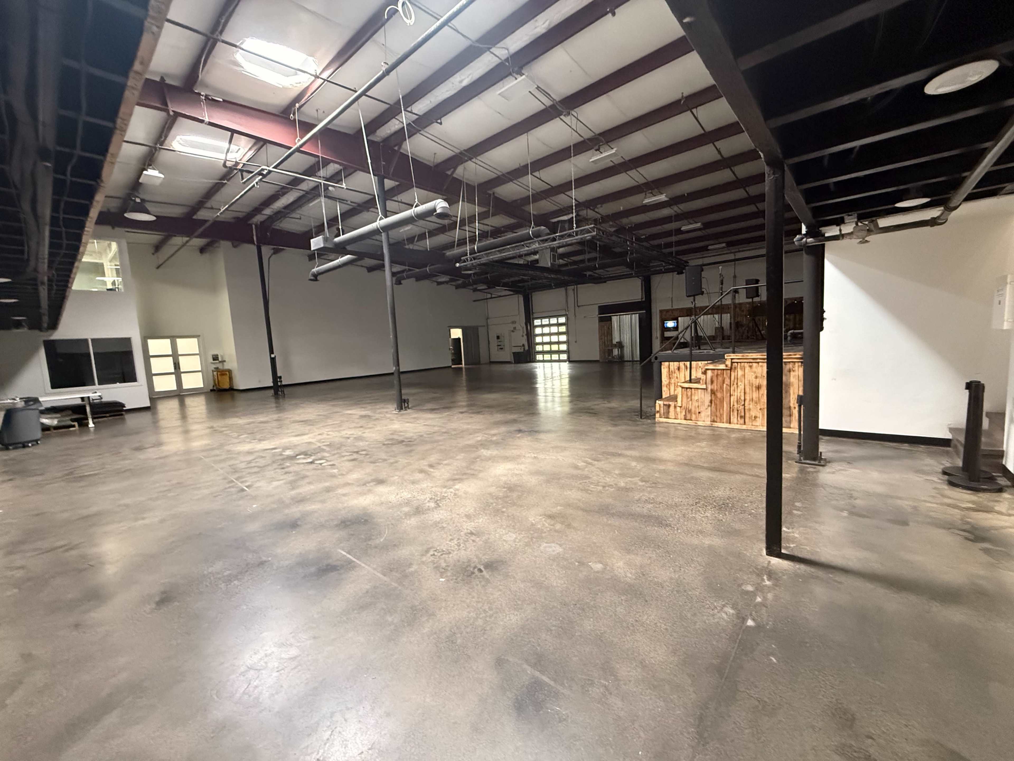The image shows a large, empty industrial space with high ceilings, polished concrete floors, and minimal furnishings.