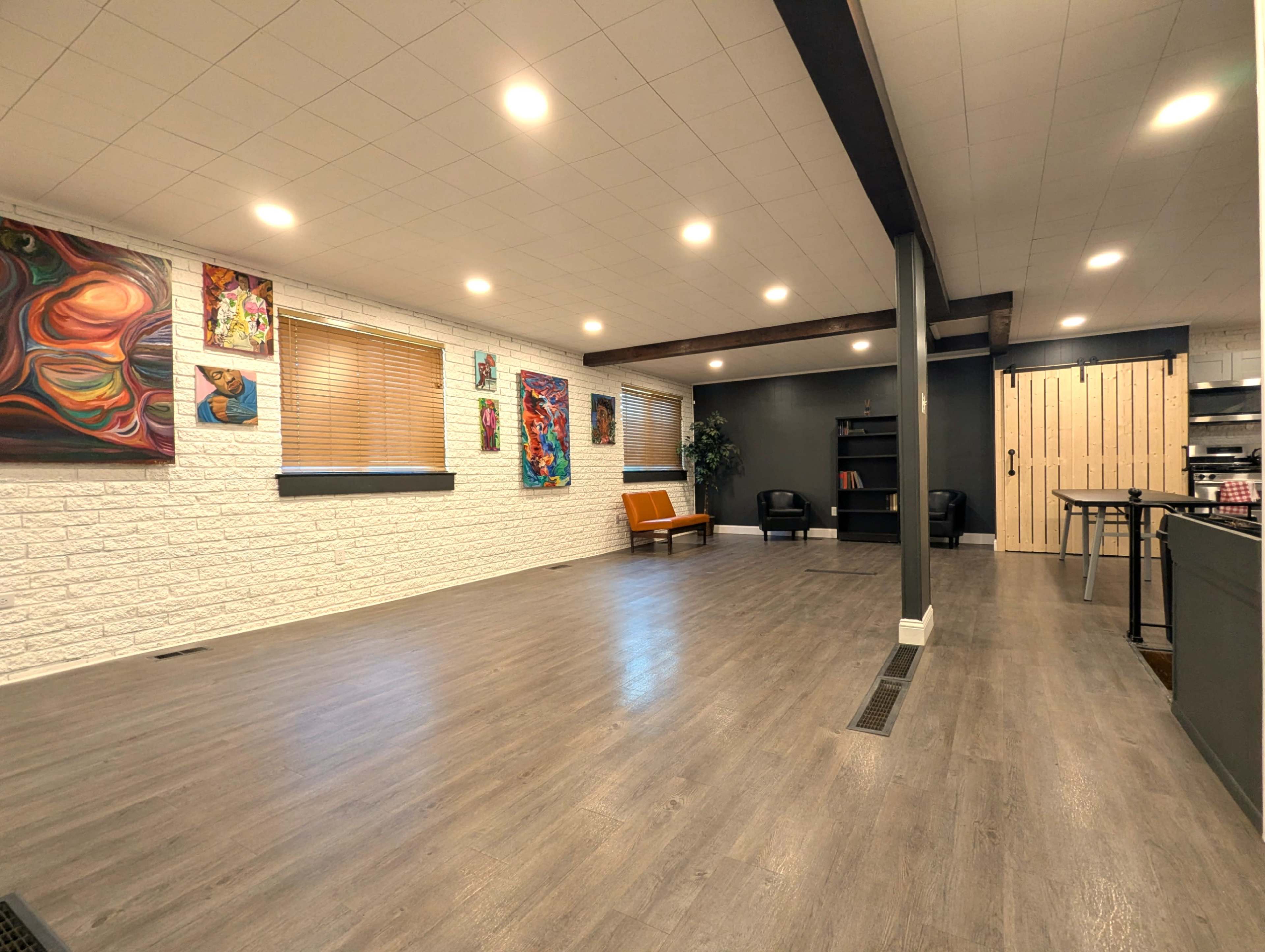 The image shows a spacious, well-lit interior with artwork on the walls, a seating area, and an open layout.