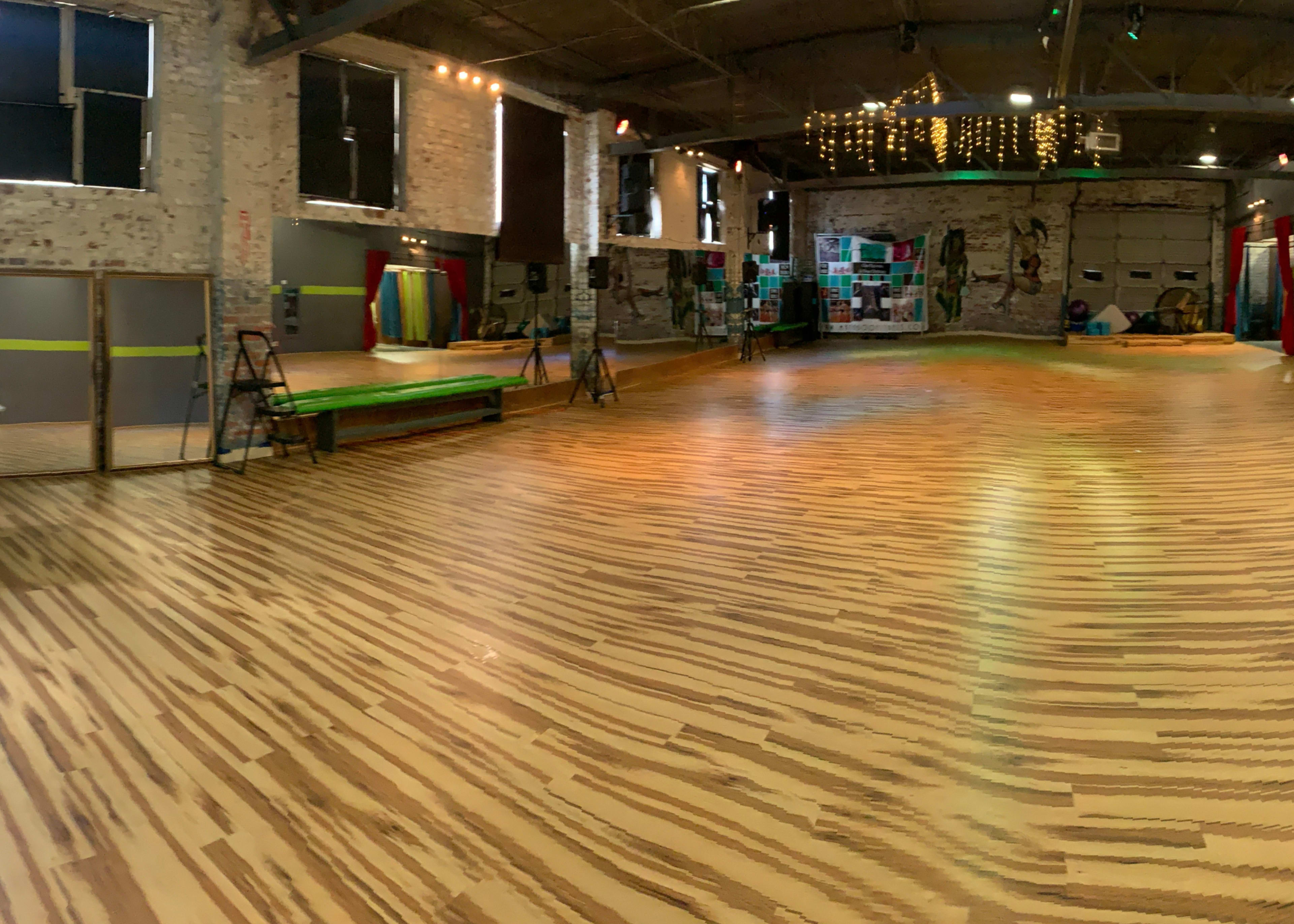 A spacious dance studio with wooden flooring, exposed brick walls, and colorful decor.