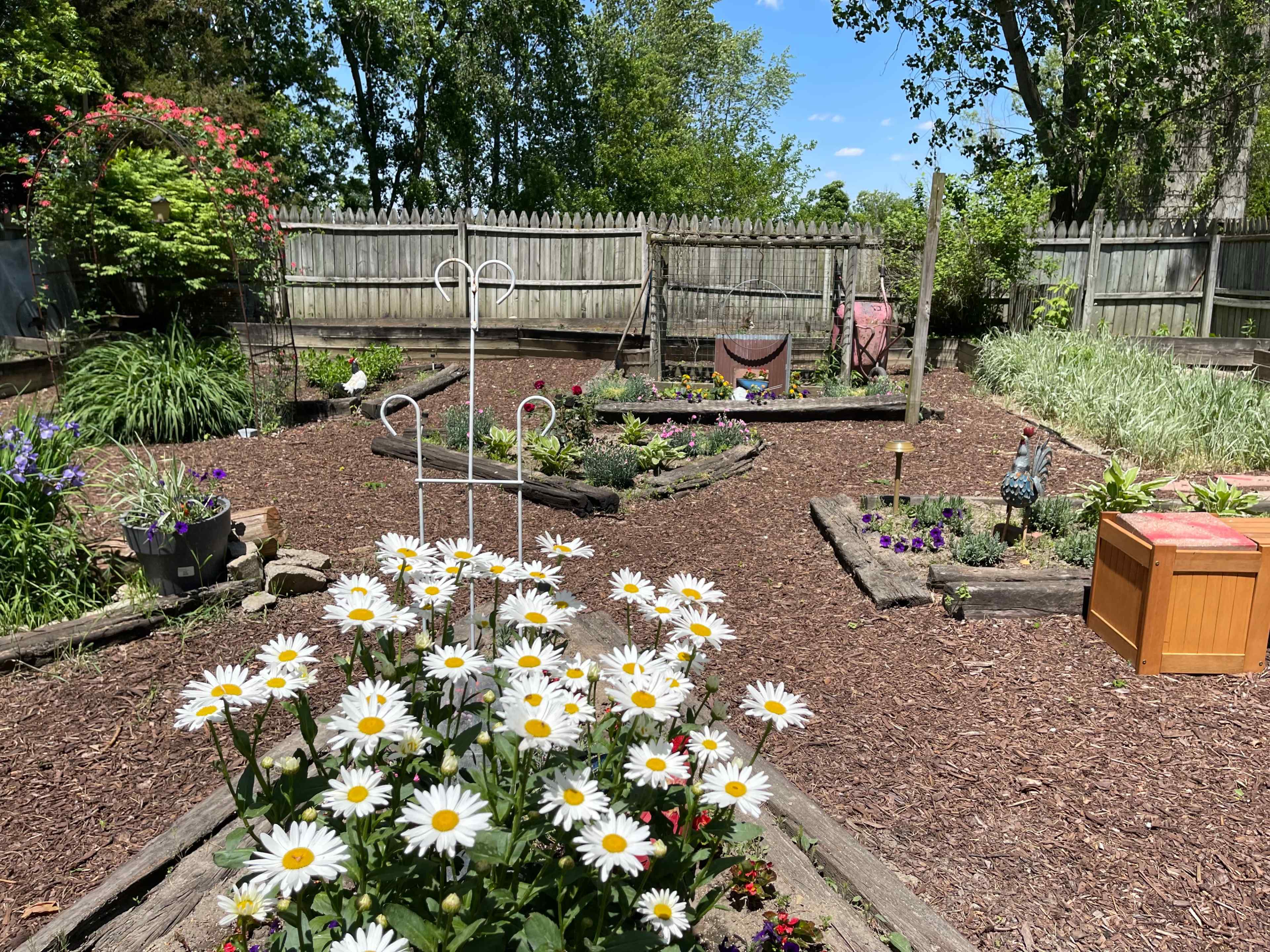 A garden layout with pathways, wooden borders, colorful flowers, and a small wooden storage box under a blue sky.